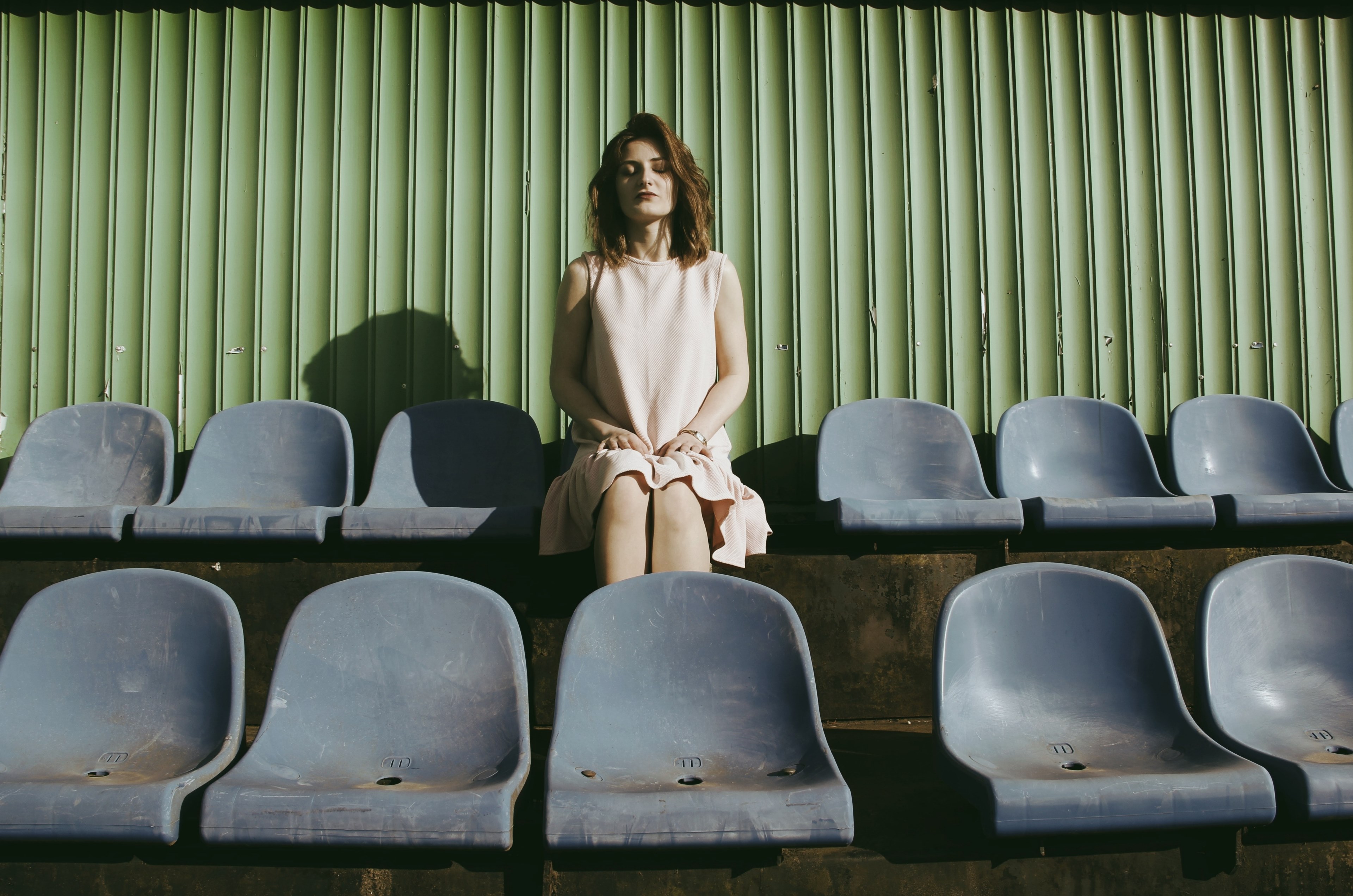 a woman in a dress sits in a row of chairs before a green wall, woman sitting in row of chairs 4k, HD Wallpaper