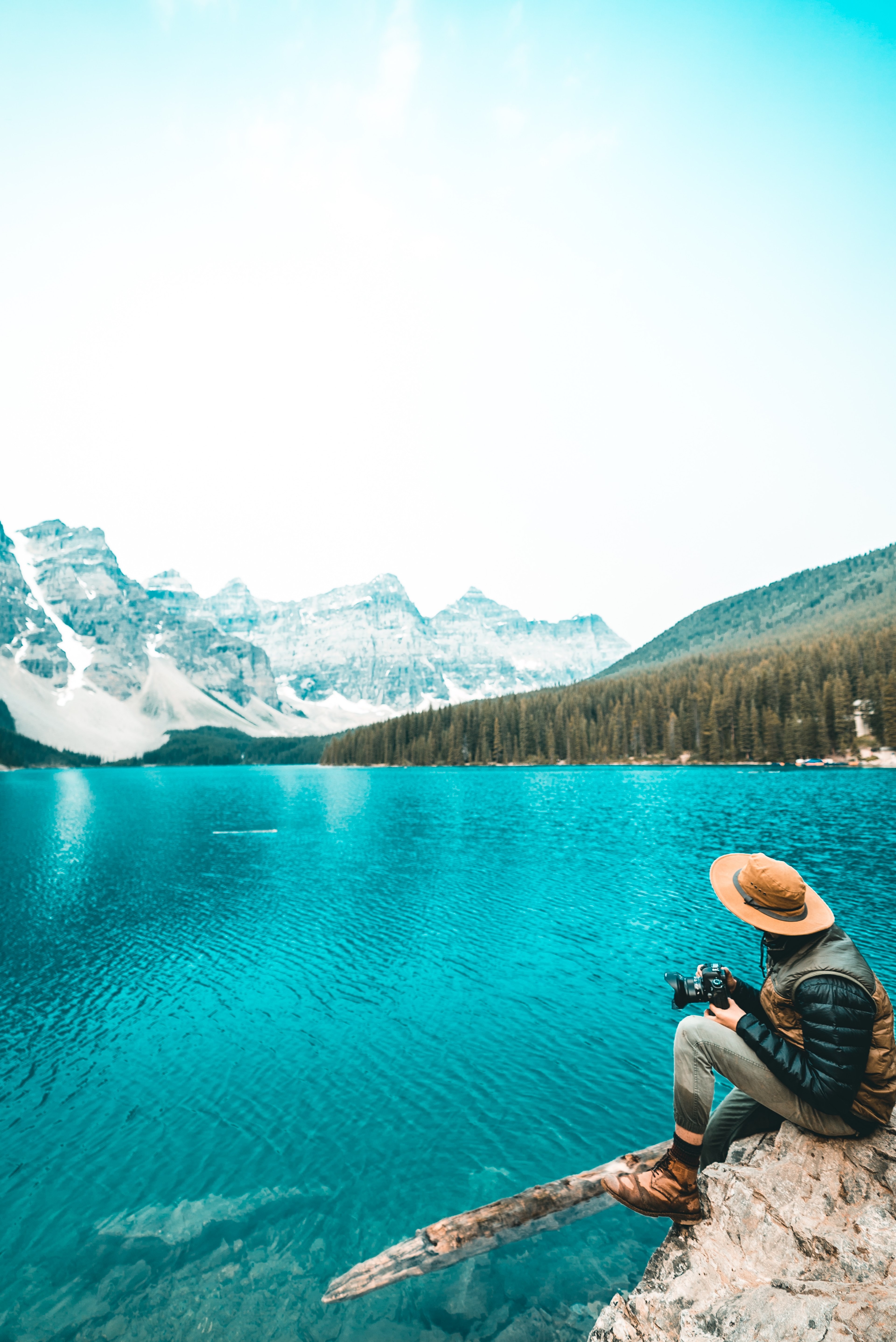 a person sitting on a rock over an azure lake and holding a camera, explore 4k, Phone HD Wallpaper