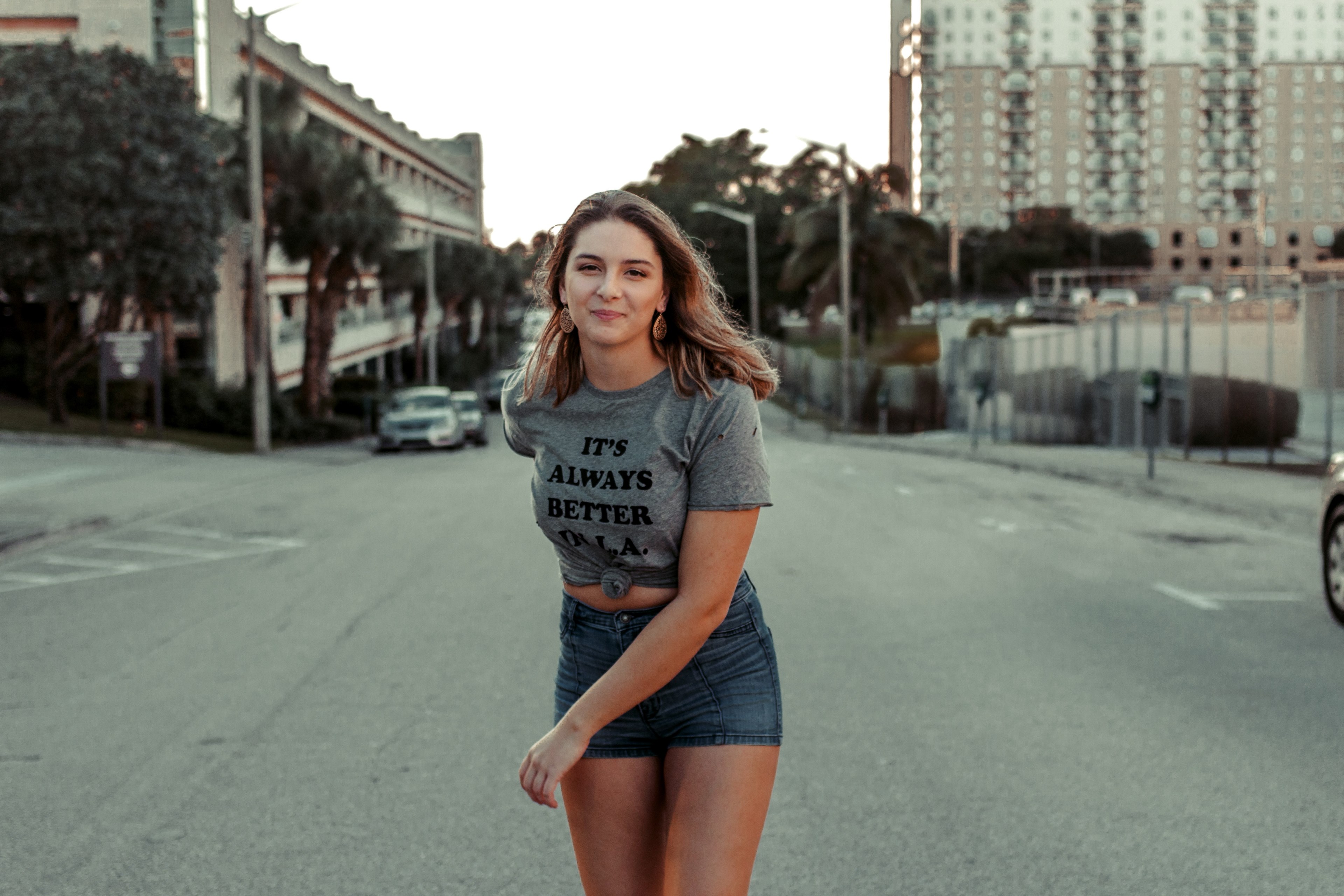 a woman stands in the street wearing a shirt reading quotits always better in laquot, its always better in la_ 4k, HD Wallpaper