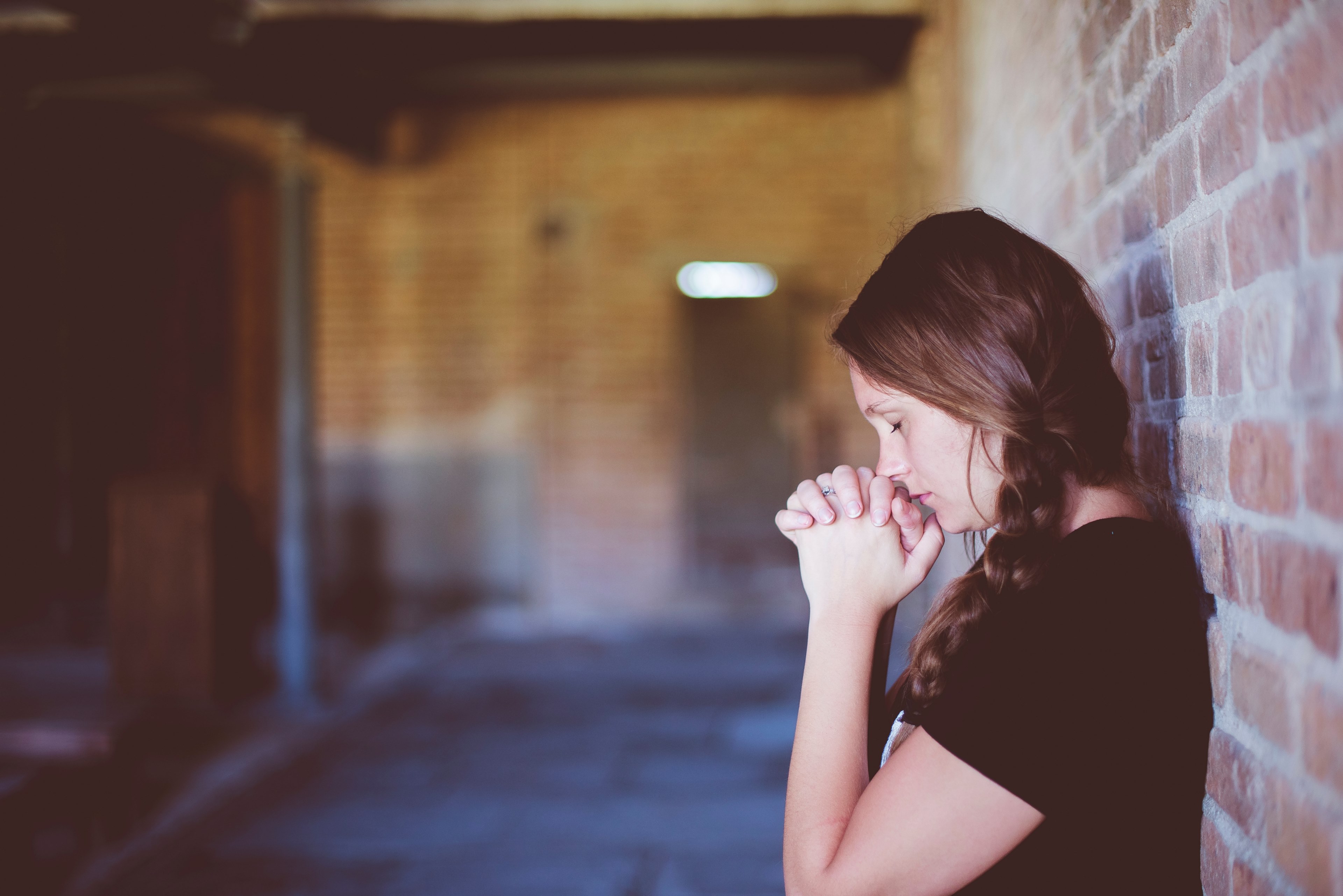 a woman wearing a braid in her hair is leaning against a brick wall praying, praying woman 4k, HD Wallpaper