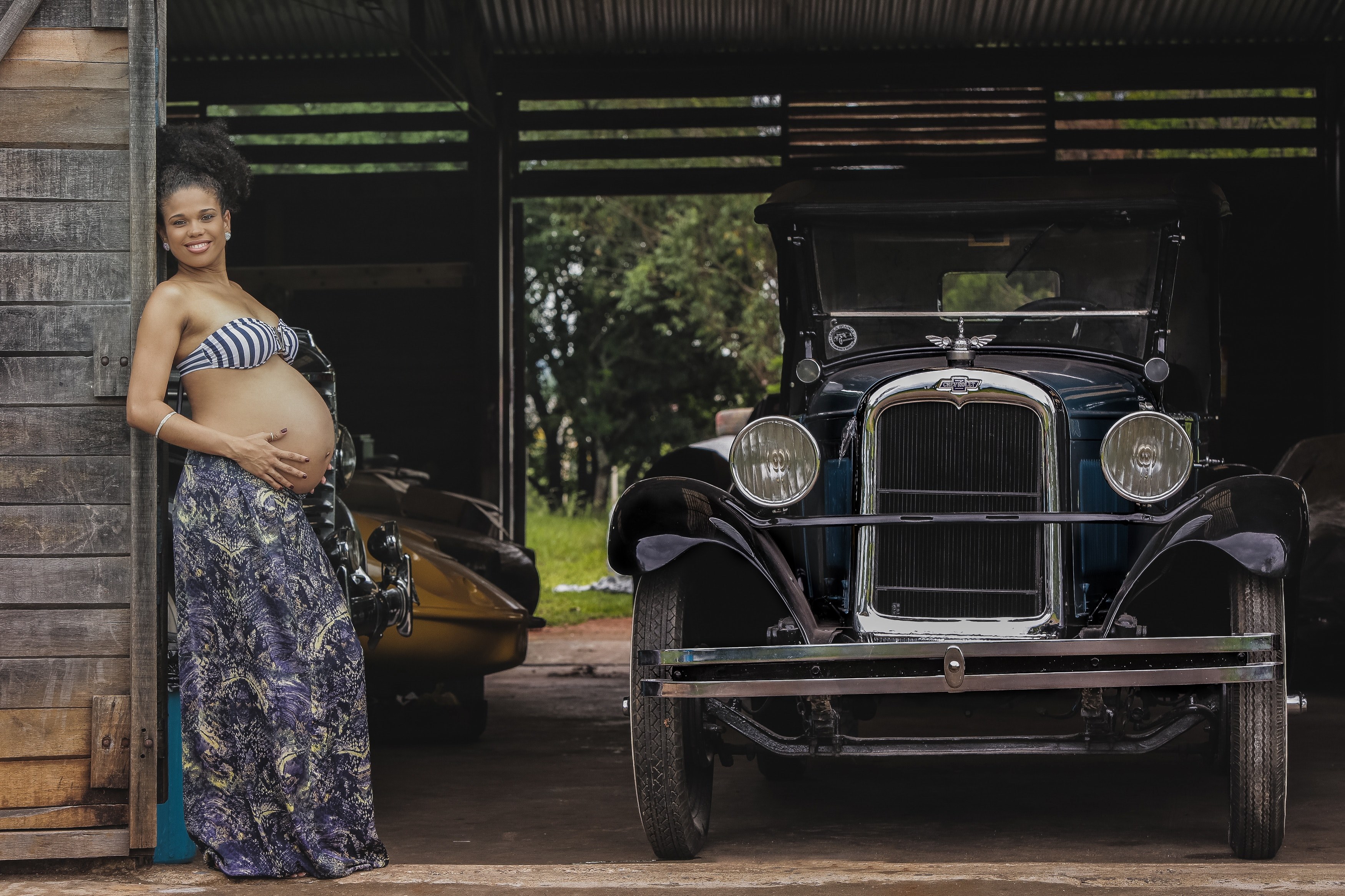 smiling pregnant woman in brasilia leaning against a wooden garage wall next to an antique chevrolet, pregnant woman and vintage car 4k, HD Wallpaper