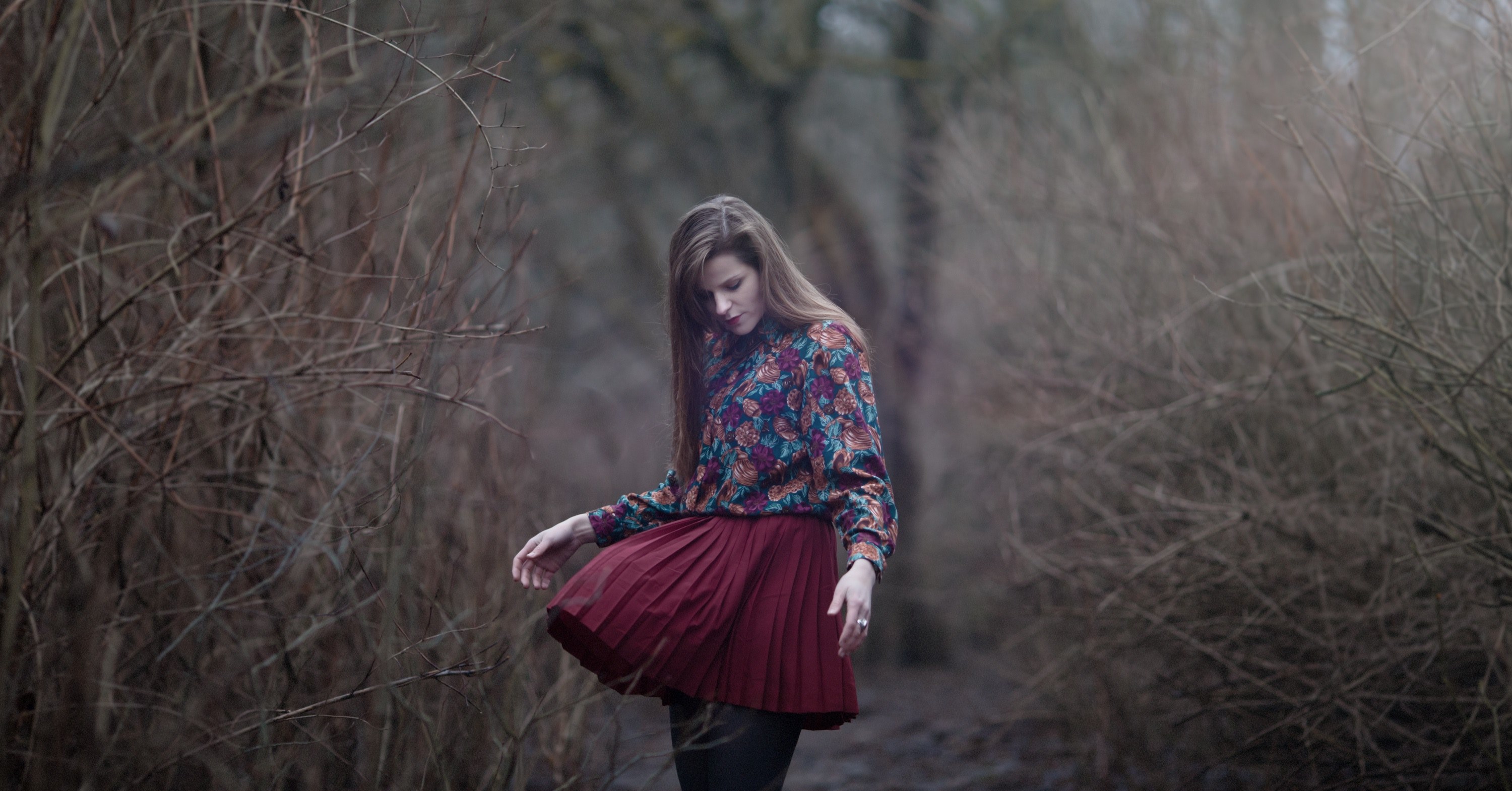 a woman looks down at her billowing skirt on a path among dead trees in vilnius, wind 4k, HD Wallpaper