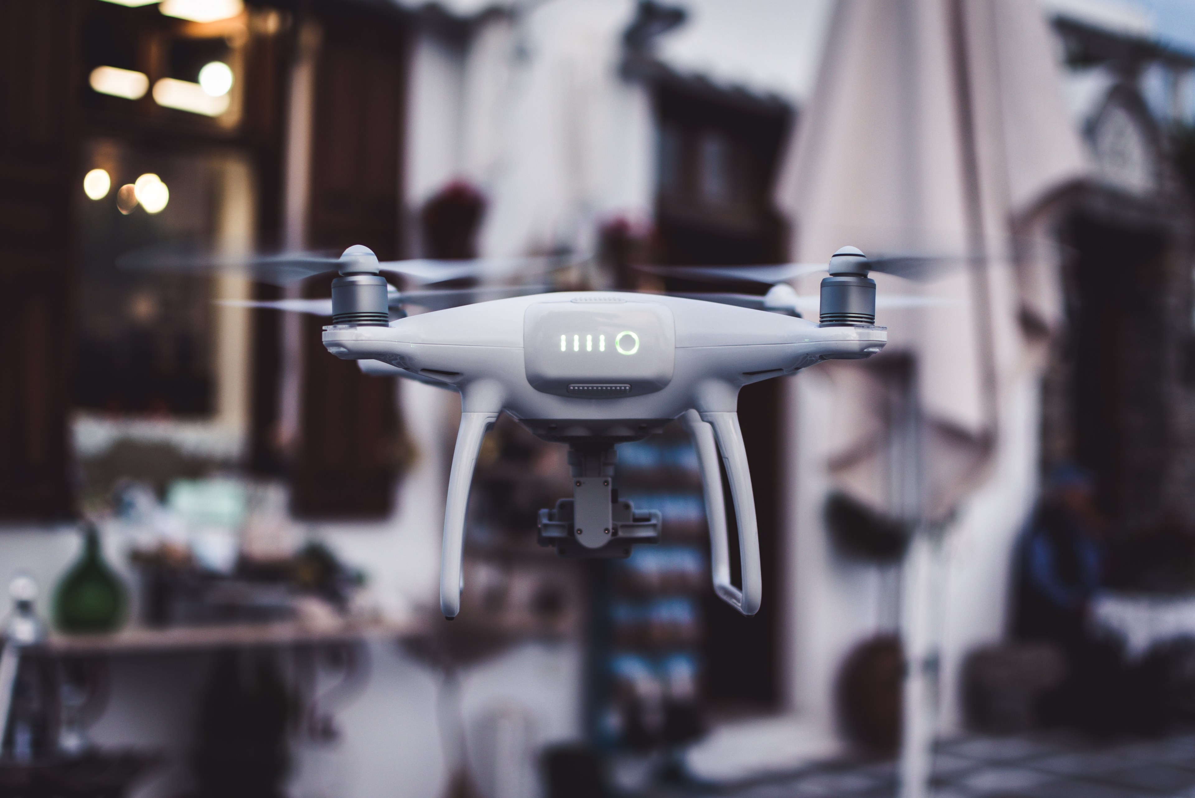 a white drone hovering in front of a white home with brown shutters and doorway beside a patio umbrella, white drone hovering 4k, HD Wallpaper