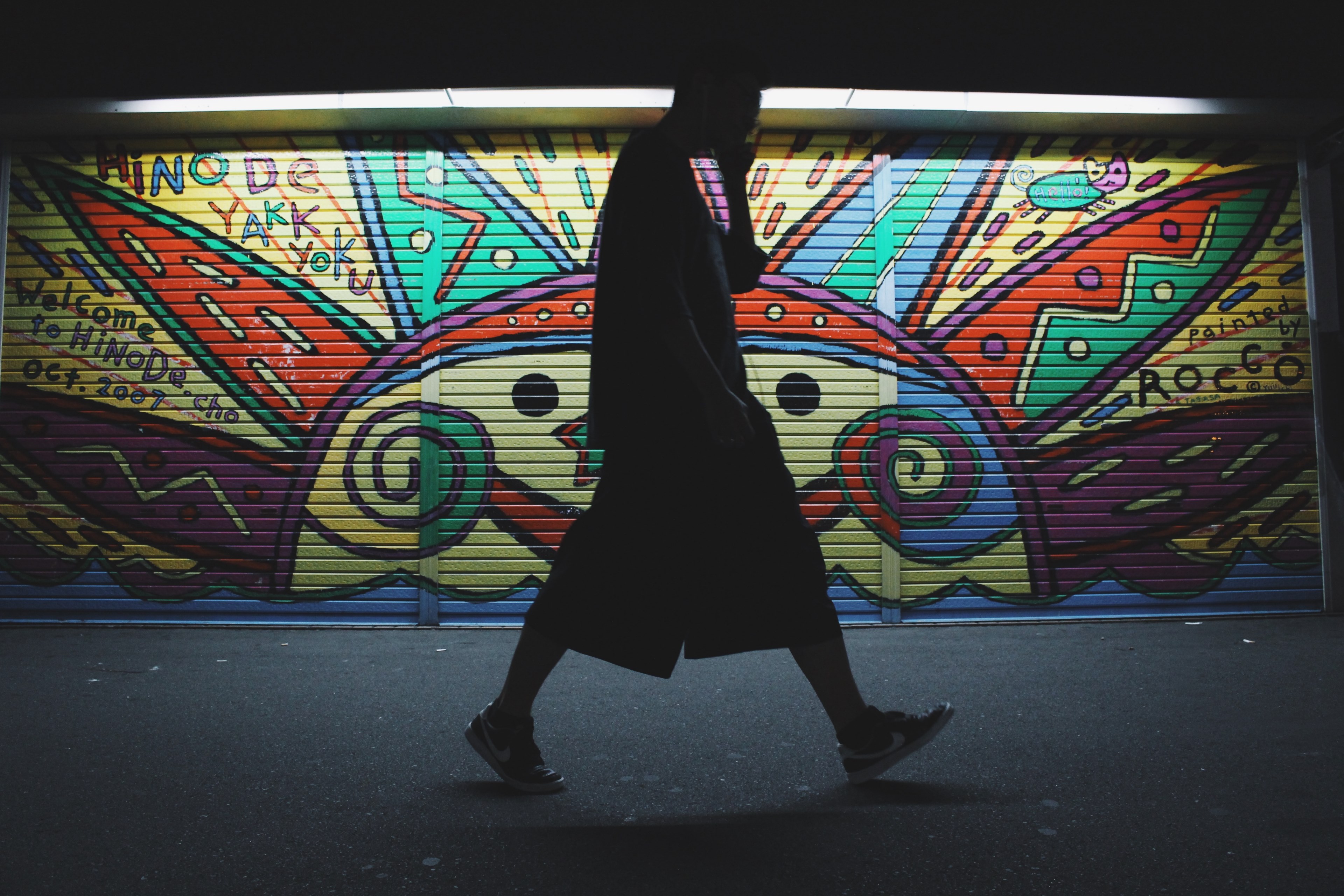 silhouette of man in shorts and t shirt on phone walking past colorful sun graffiti art, person in front of garage graffiti 4k, HD Wallpaper