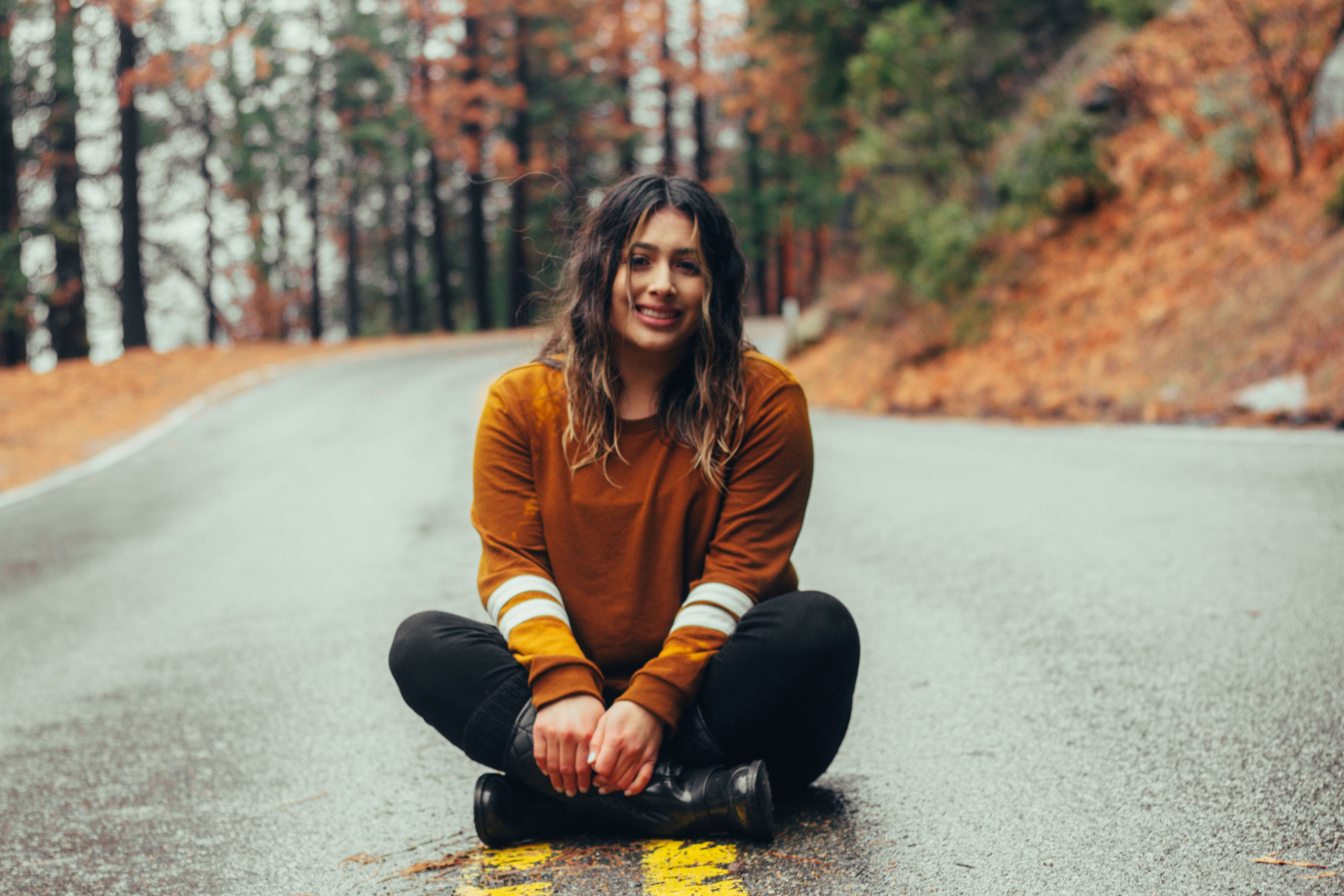 a woman with wavy hair smiles while sitting cross legged on a road in yosemite national forest, smiling cross legged on road 4k, HD Wallpaper