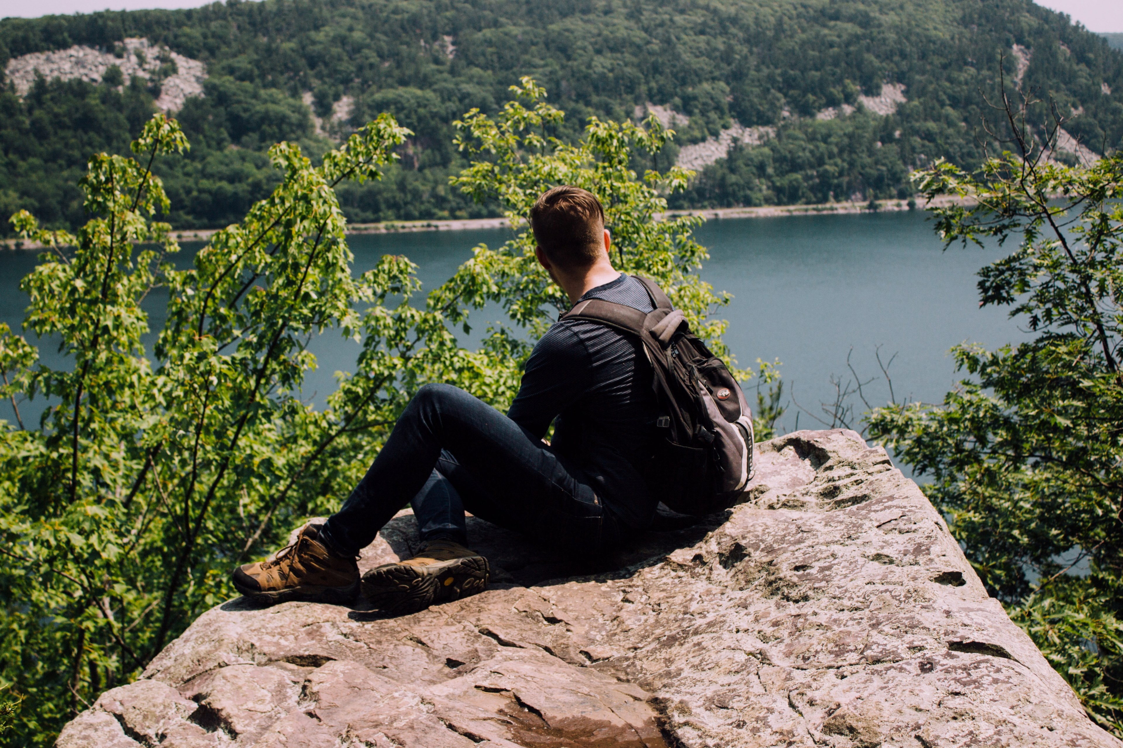 backpacker sits alone on a rocky cliff overlooking a mountain lake, backpacker over a lake 4k, HD Wallpaper
