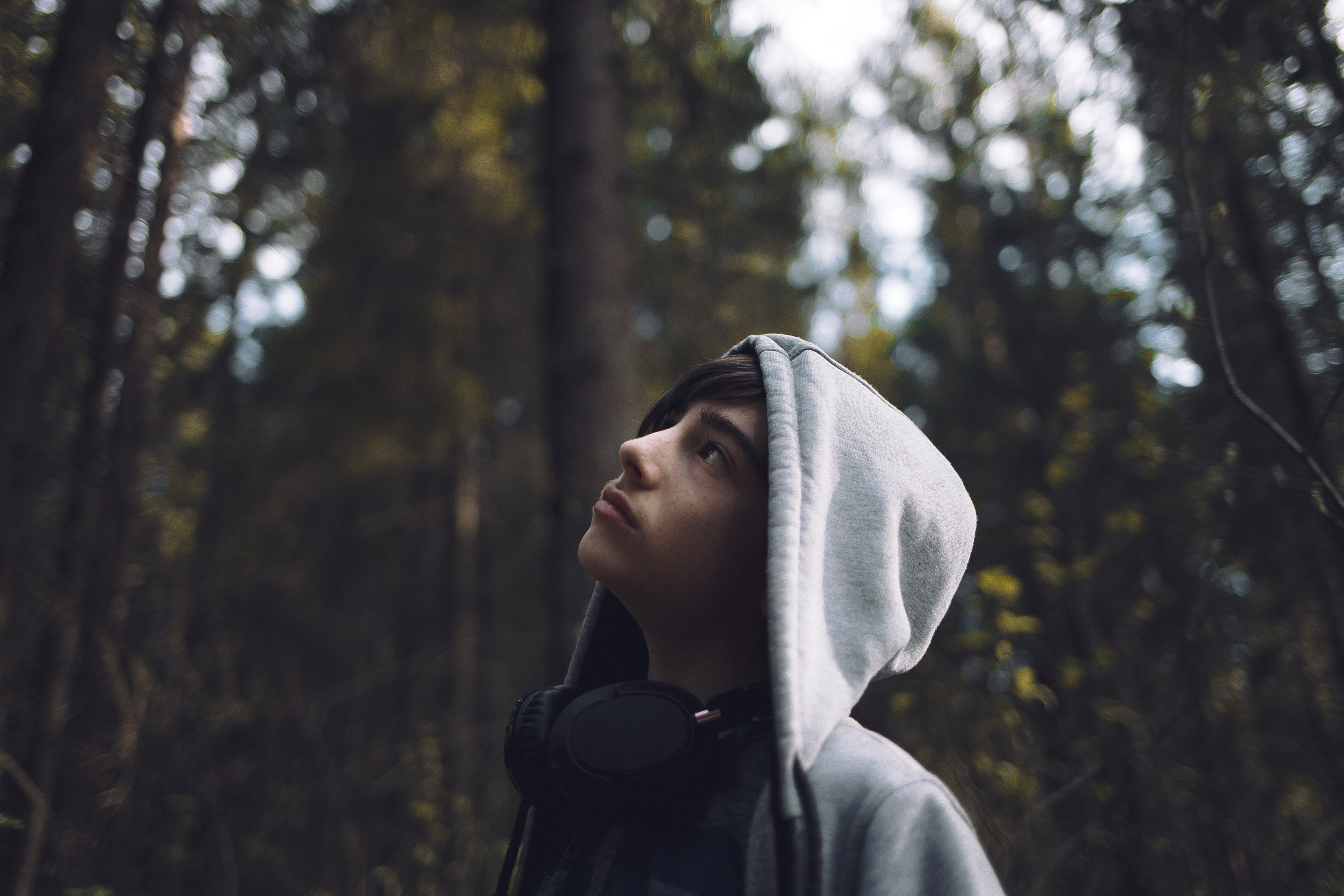 person wearing a hoodie and headphones looks up in the woods, young explorer 4k, HD Wallpaper