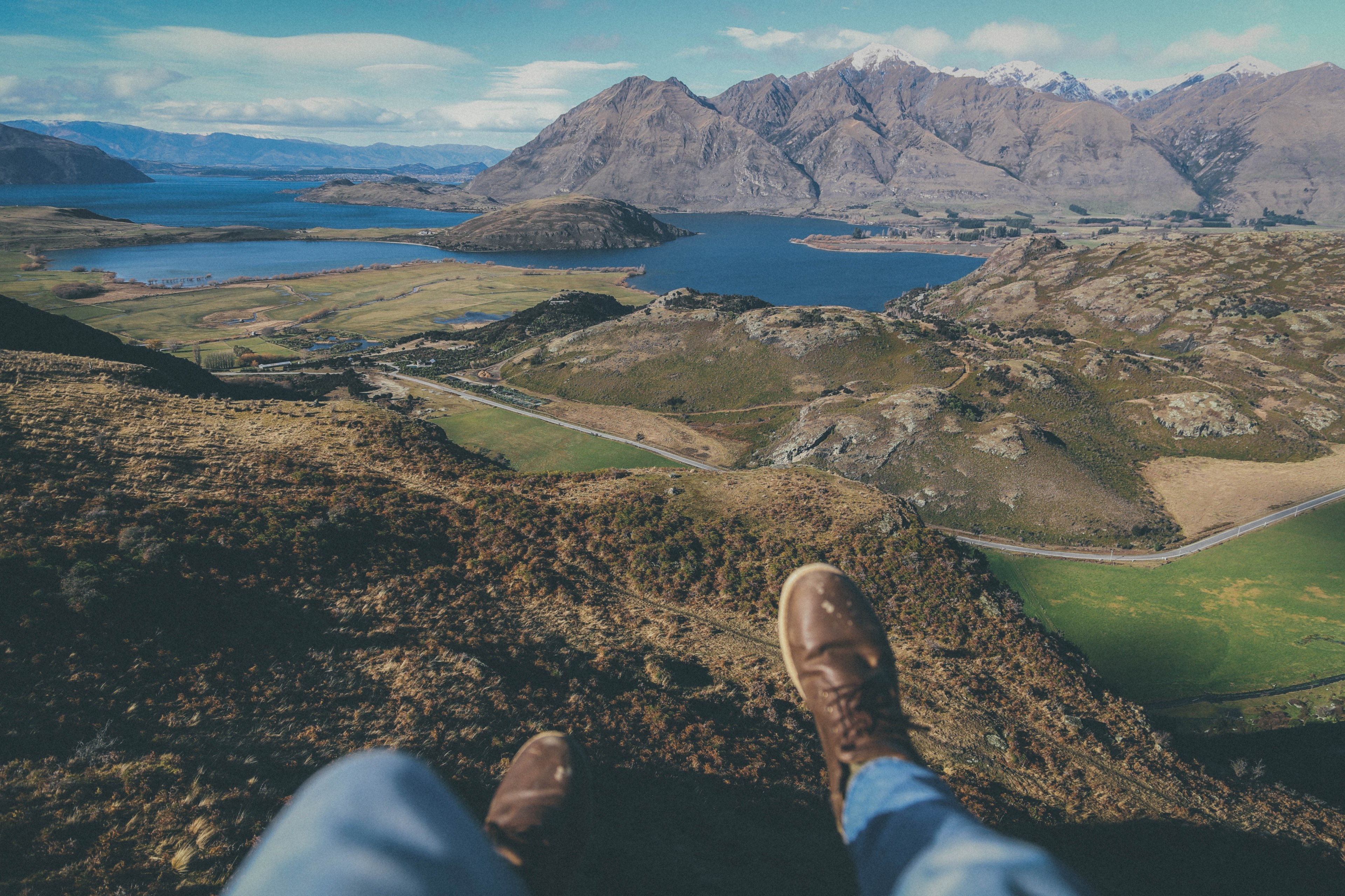 a persons legs dangling off from a hill over mountain lakes in new zealand, sitting over mountain lakes 4k, HD Wallpaper