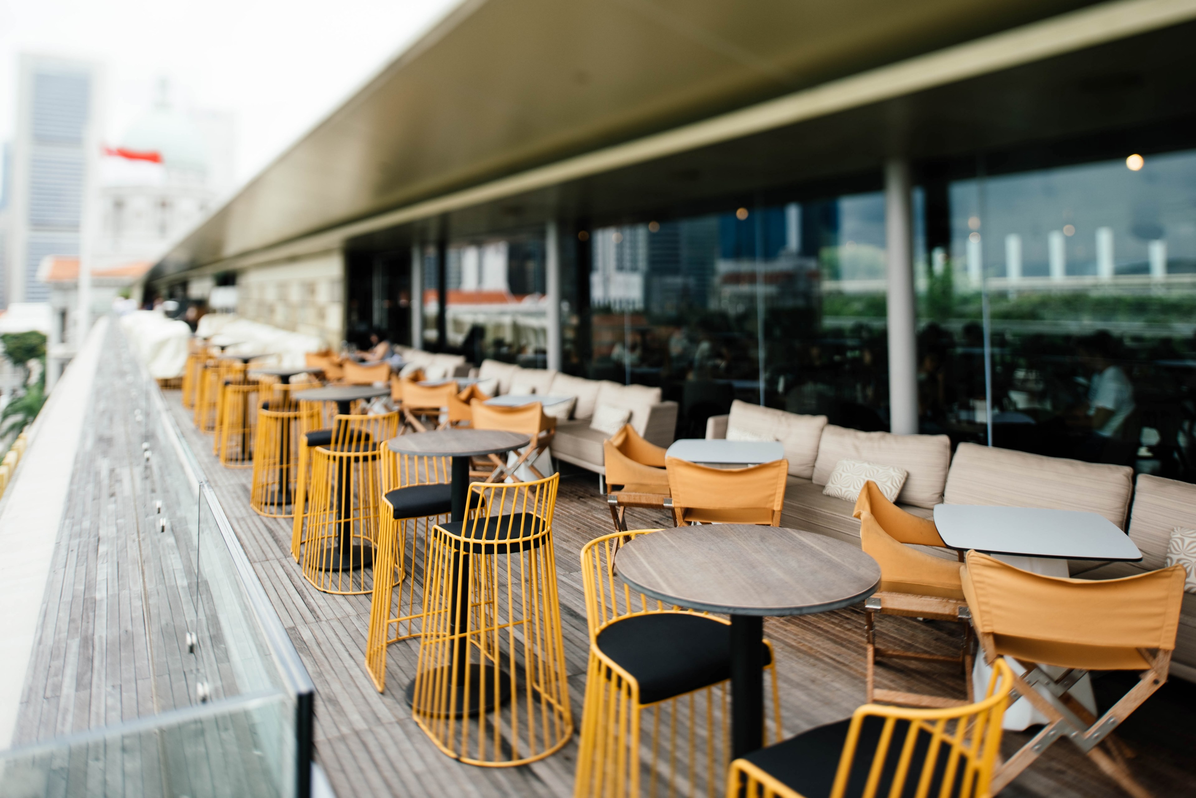 wooden deck with modern tables and yellow chairs adjacent to a long building with windows, tables and chairs on deck 4k, HD Wallpaper
