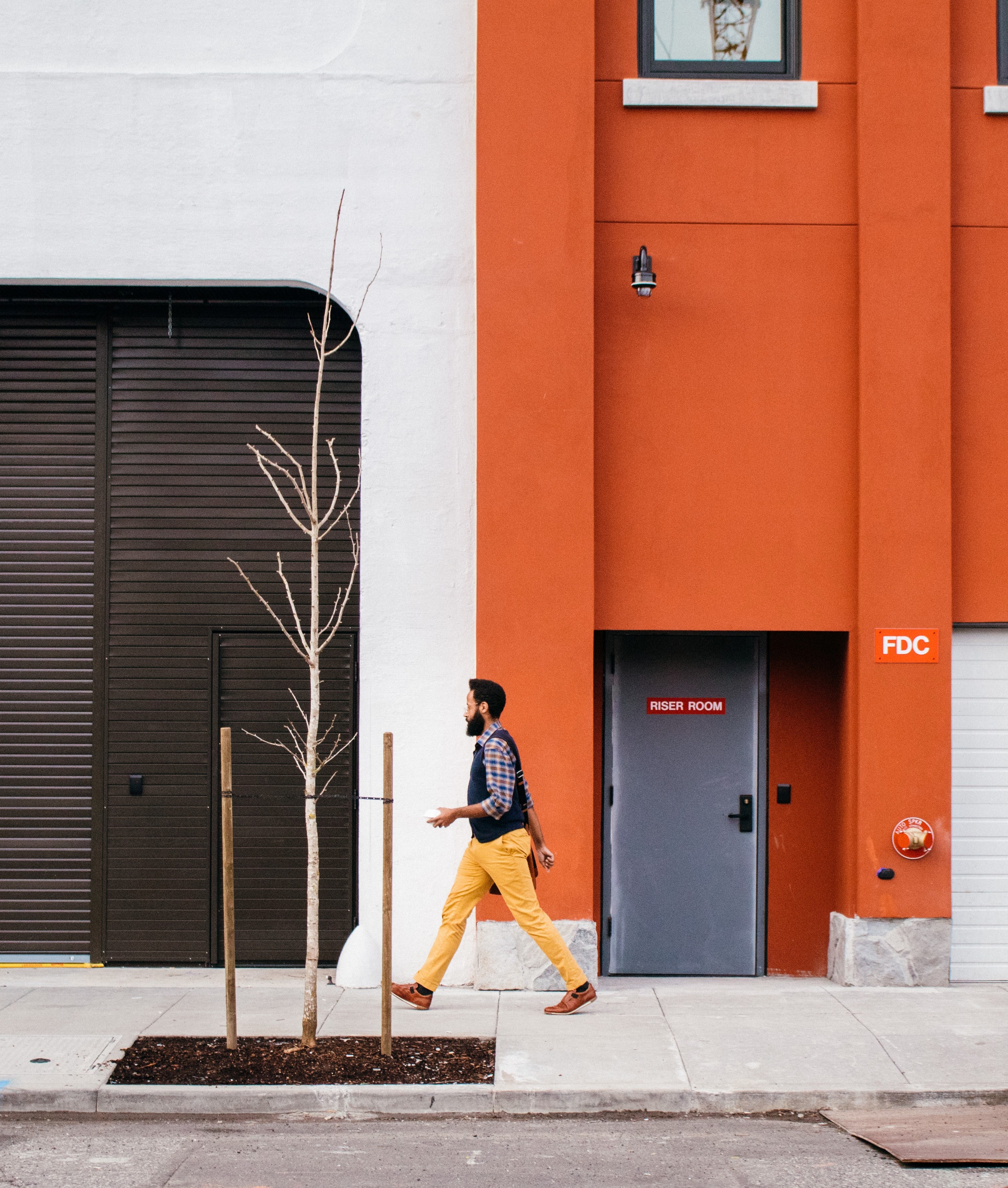 a bearded man in a vest walking on a sidewalk along an orange painted building, caught in the middle 4k, Phone HD Wallpaper