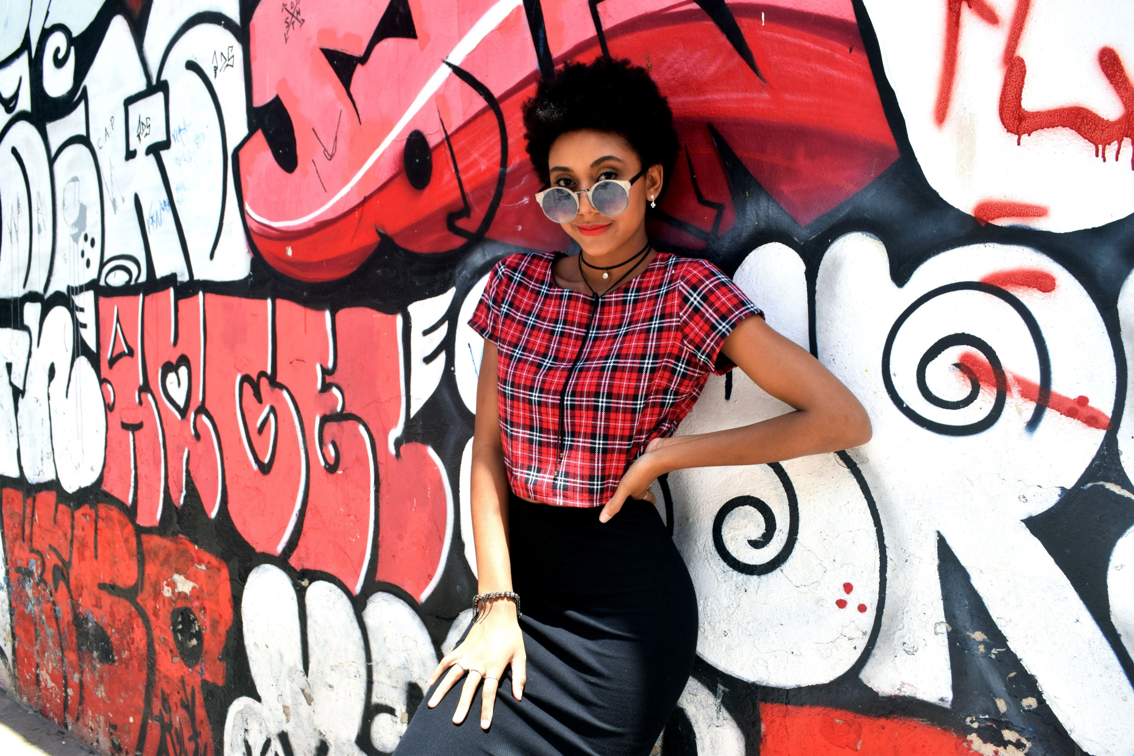 a woman in a plaid shirt leans against a black red and white graffitied wall, power 4k, HD Wallpaper
