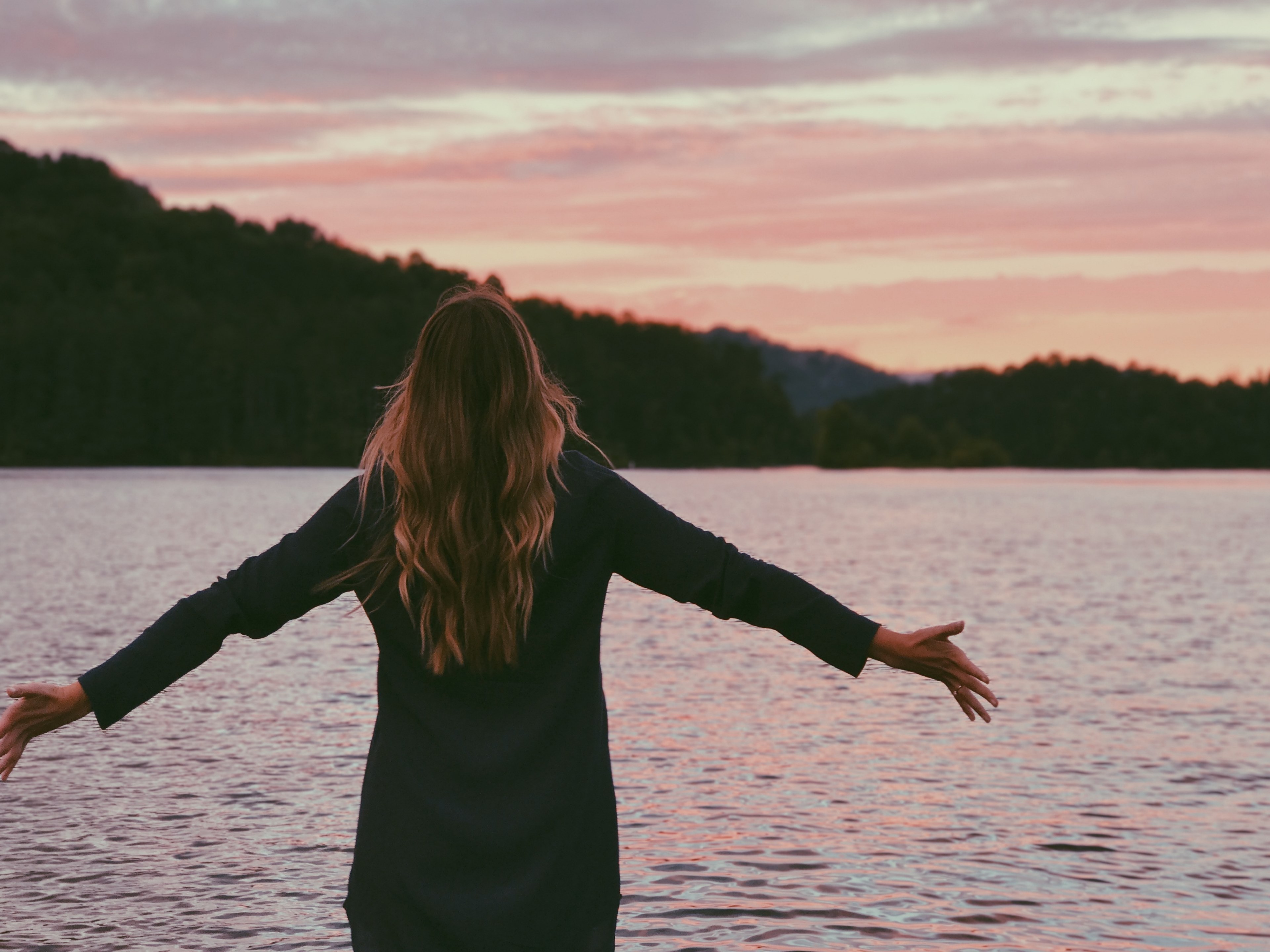 a woman faces a body of water arms outstretched at sunset, arms outstretched by the water 4k, HD Wallpaper