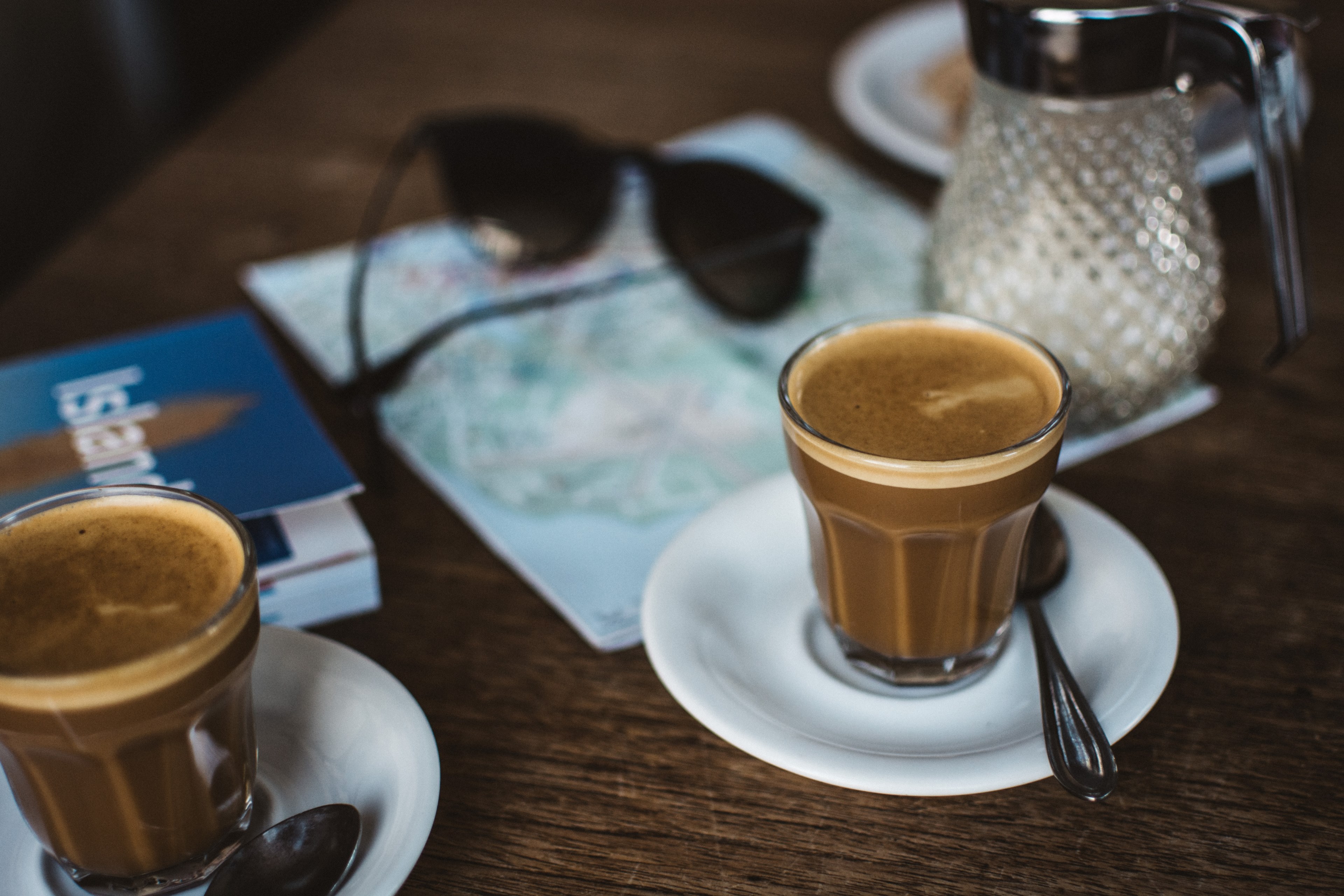 latte in a clear glass on a white saucer with a spoon with sunglasses and a map on the table, first coffee after arriving to iceland 4k, HD Wallpaper