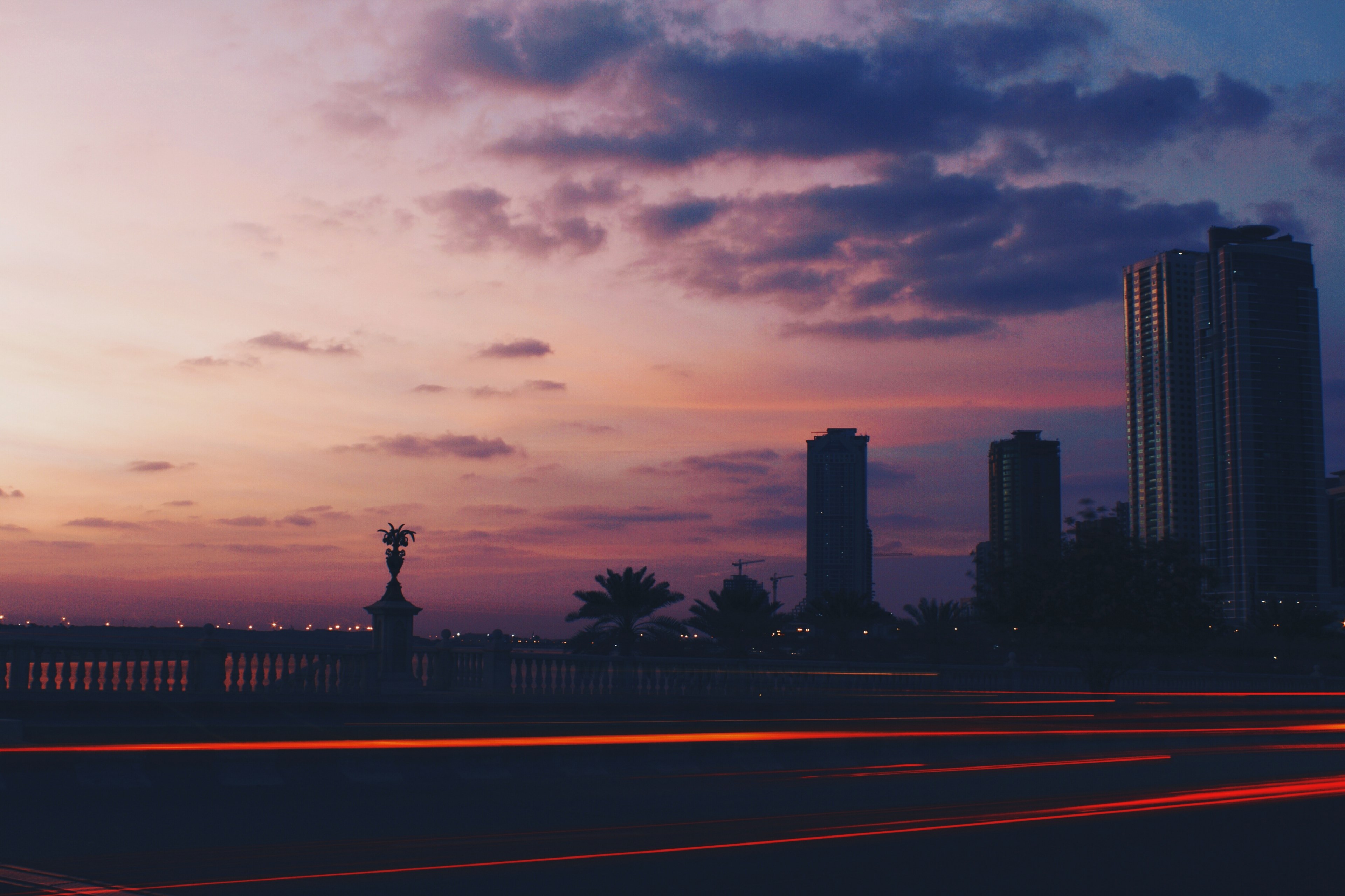 a city skyline plants and railing against pink and purple skies red lights trailing with long exposure effect, sunset vibes 4k, HD Wallpaper