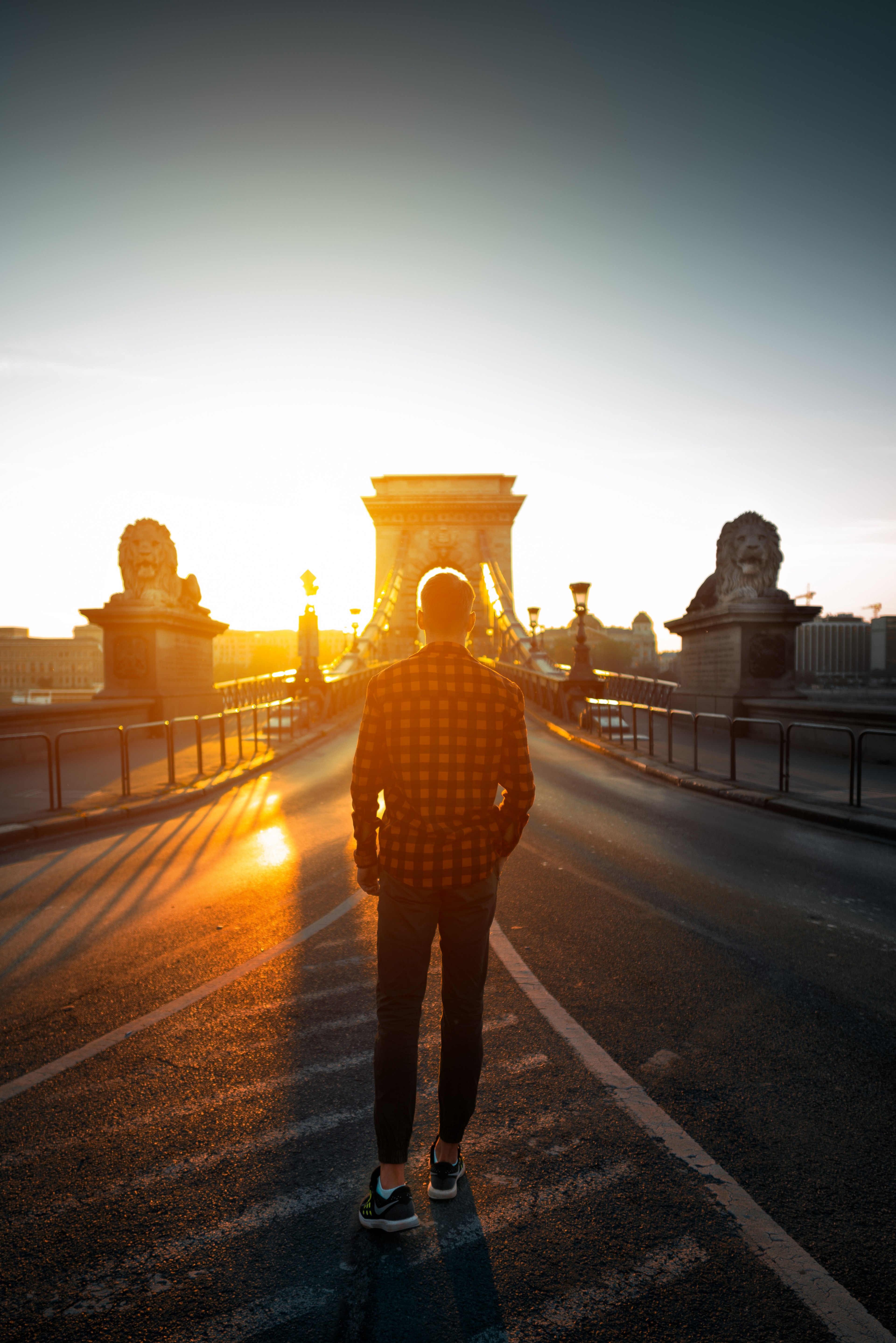 a man walks towards the szchenyi chain bridge in the middle of the road as the sunrise or sunset lights the sky yellow, morning vibe 4k, Phone HD Wallpaper