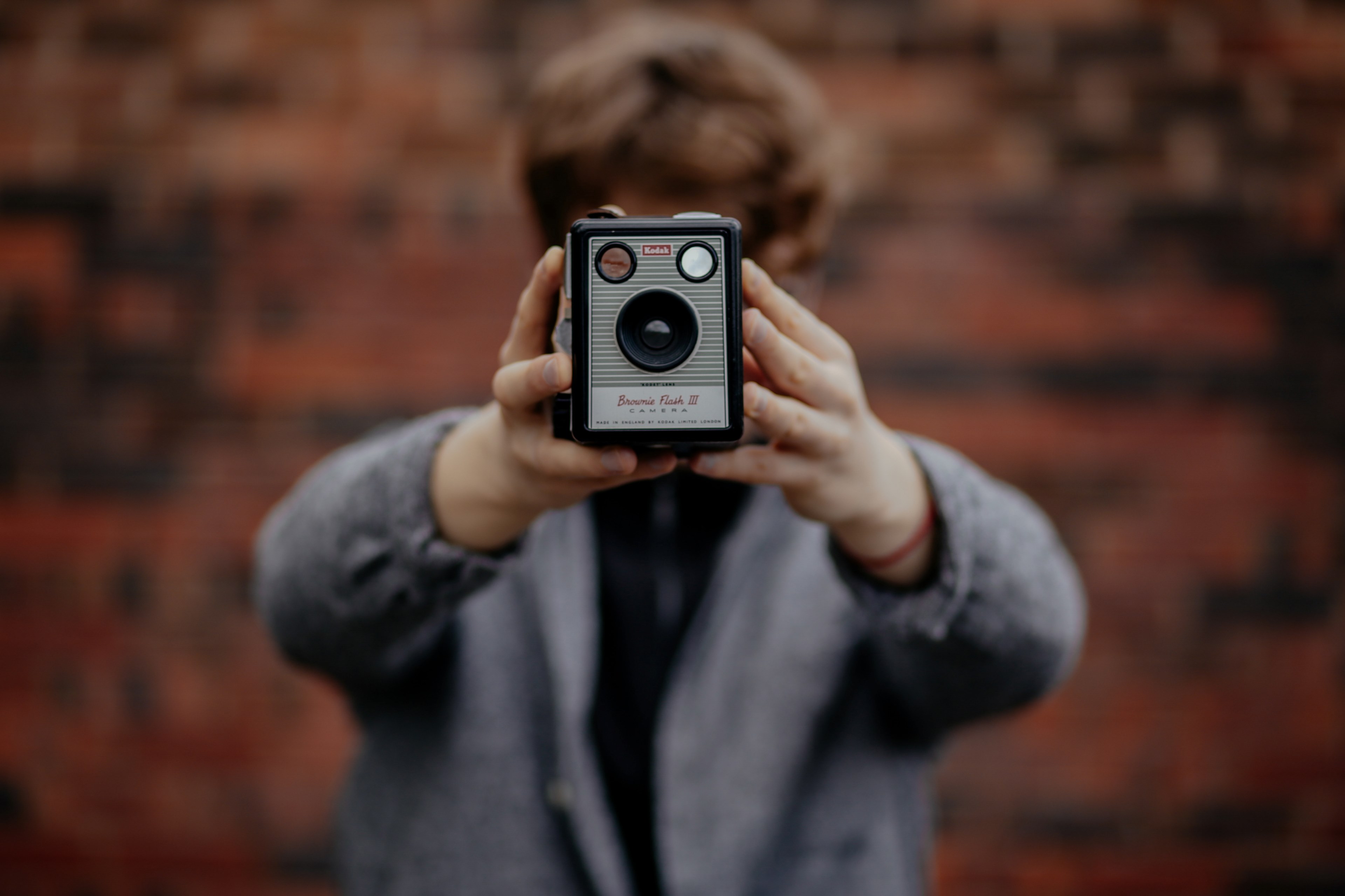 a person with short brown hair and a gray sweater taking a selfie with a vintage kodak camera covering his face, selfie with vintage camera 4k, HD Wallpaper