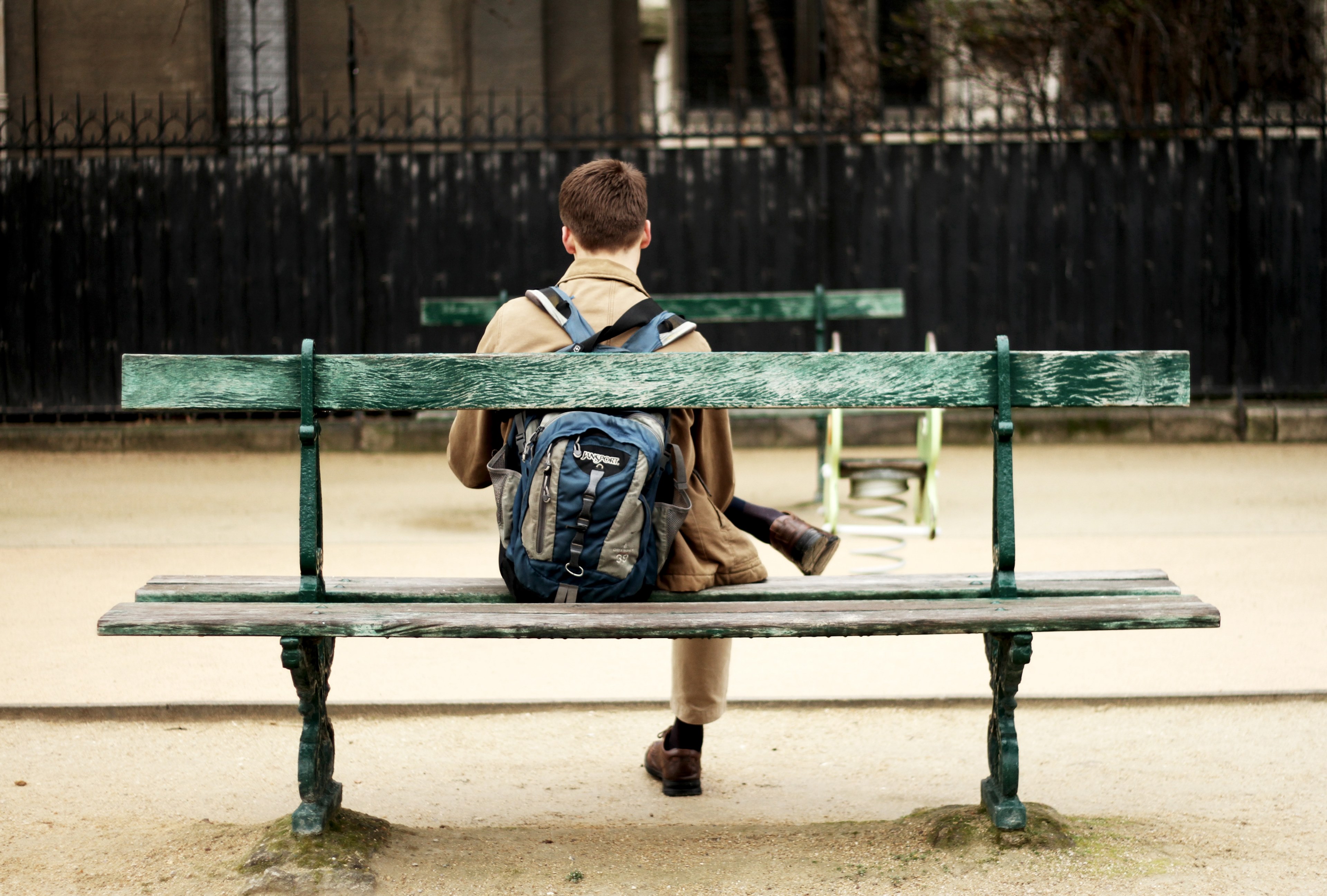 a person in a backpack sits on an outdoor bench crossing their legs, person sitting on a bench 4k, HD Wallpaper