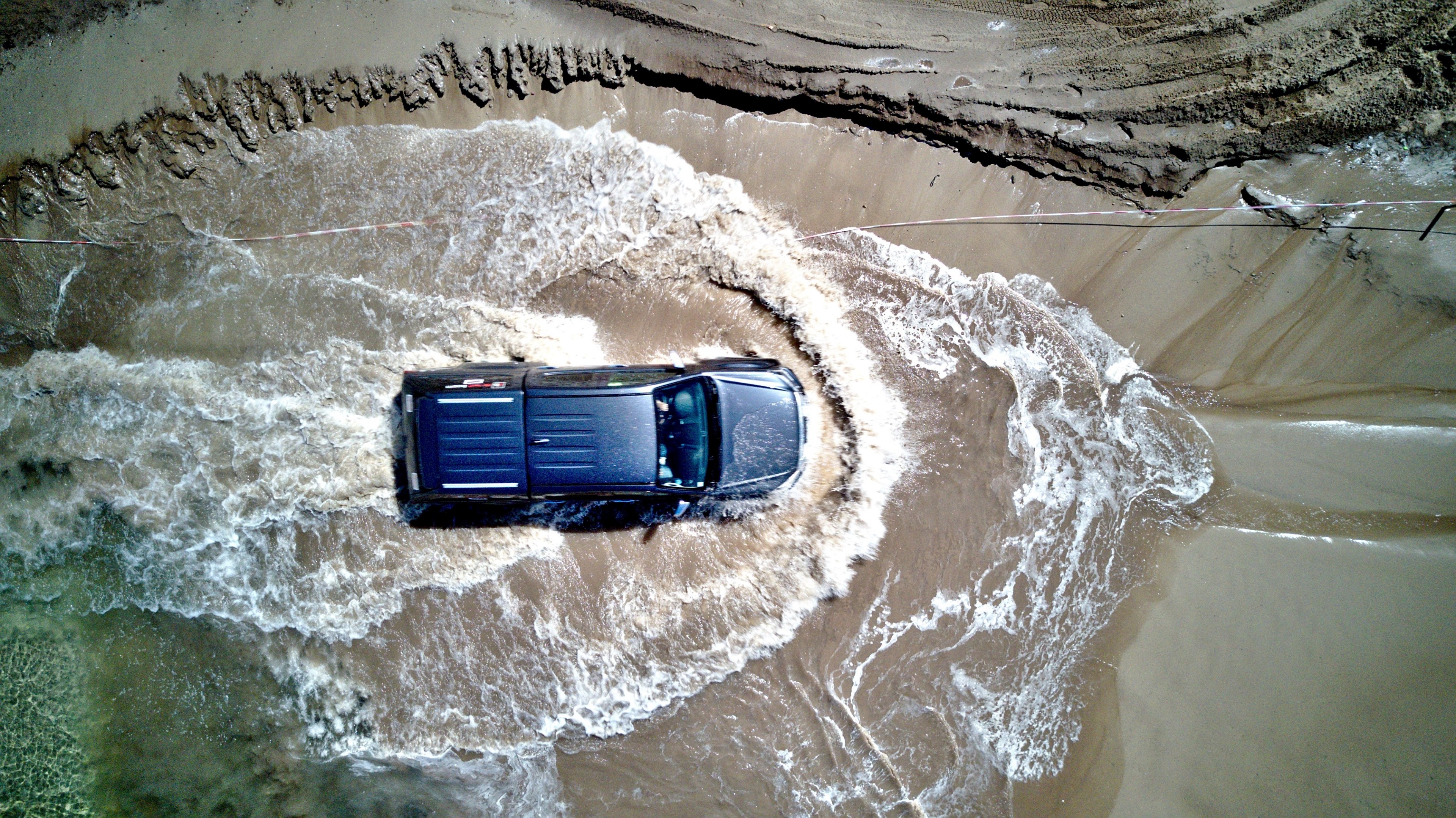 drone view of the 4x4 suv driving through the water on the sand beach at loon op zand north brabant netherlands, splitting the waters 4k, HD Wallpaper