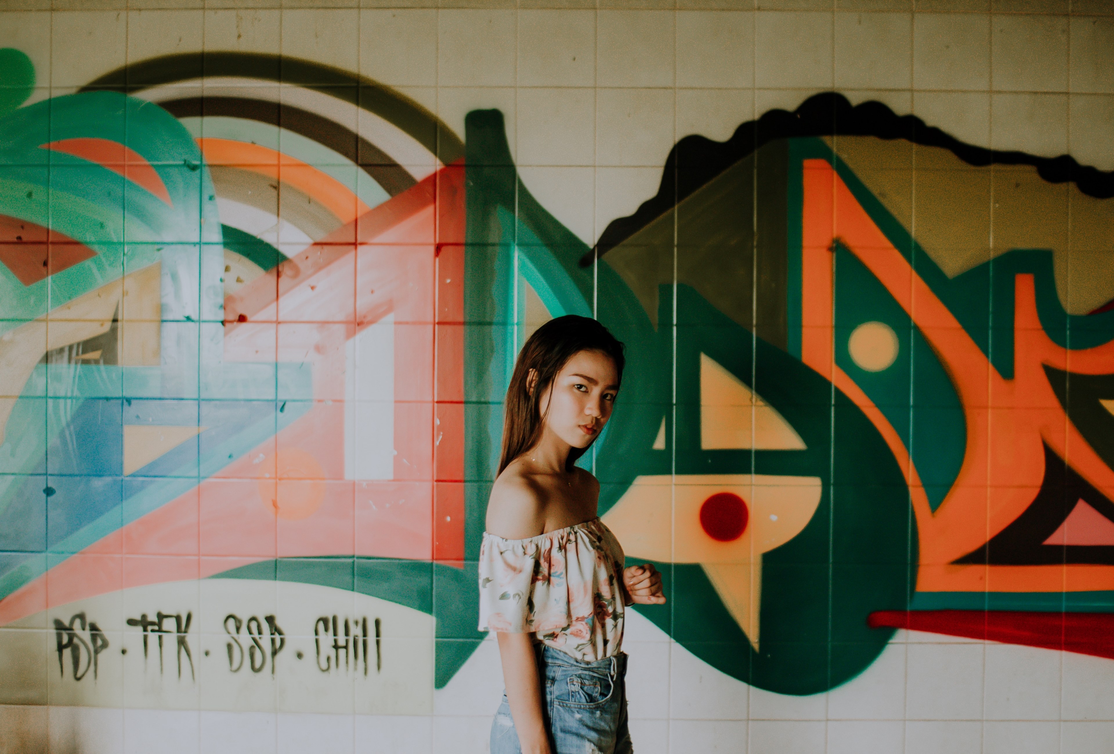 a young woman in an off shoulder top looks at the camera against a graffiti wall, _woman with graffitied tiles 4k, HD Wallpaper