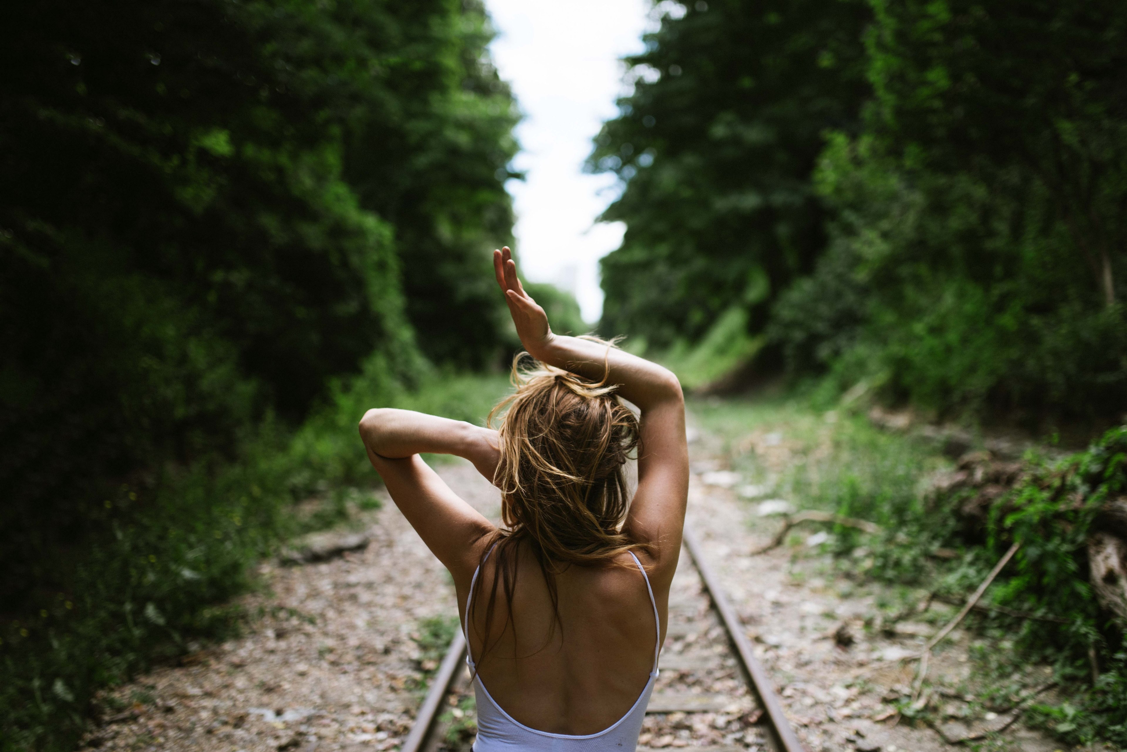 a woman faces away down outdoor train tracks in paris with her arms over her head, lost in the wilderness 4k, HD Wallpaper