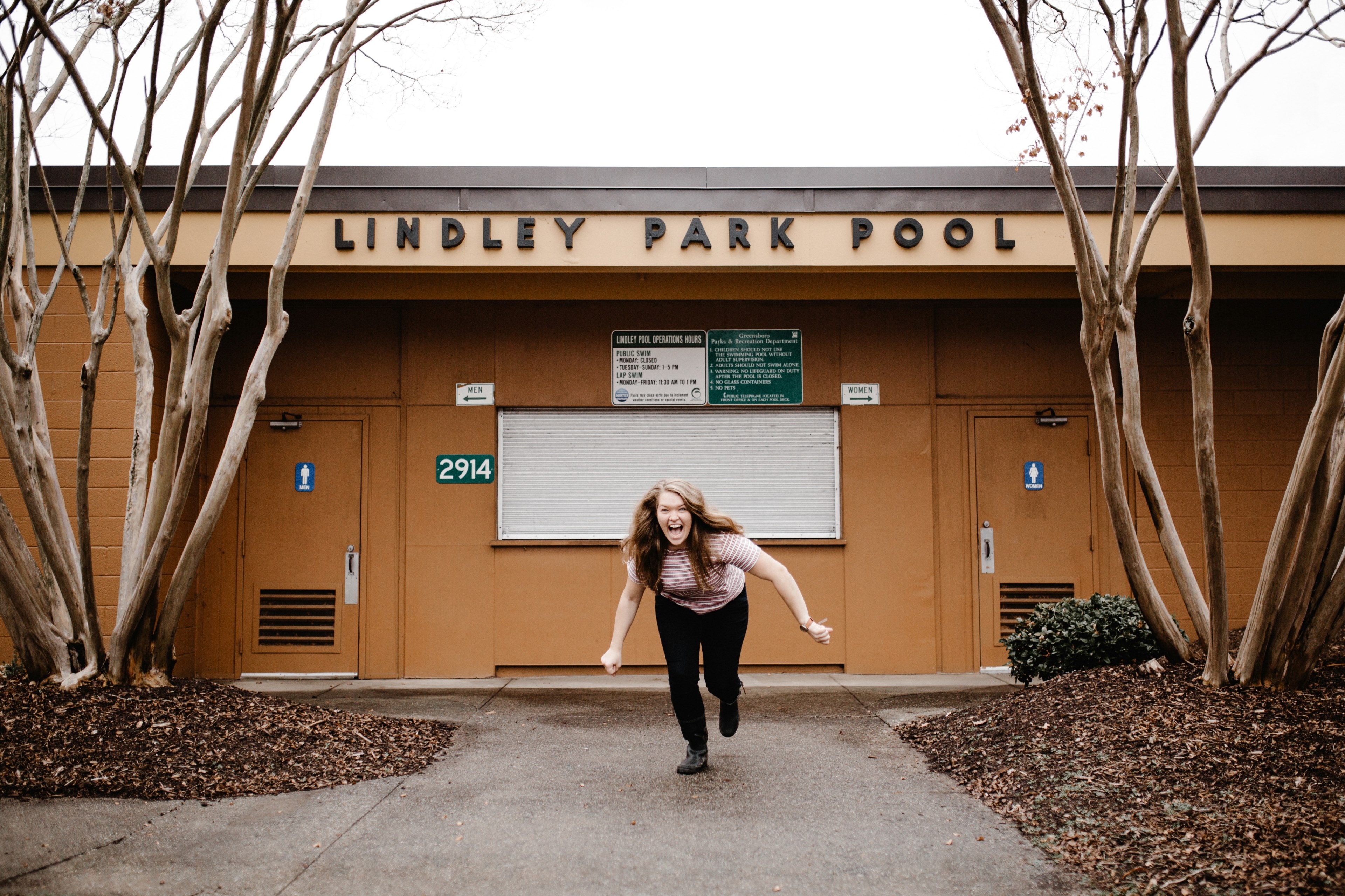 a woman laughs while lunging forward in front of the bathrooms at the lindley park pool, be happy 4k, HD Wallpaper