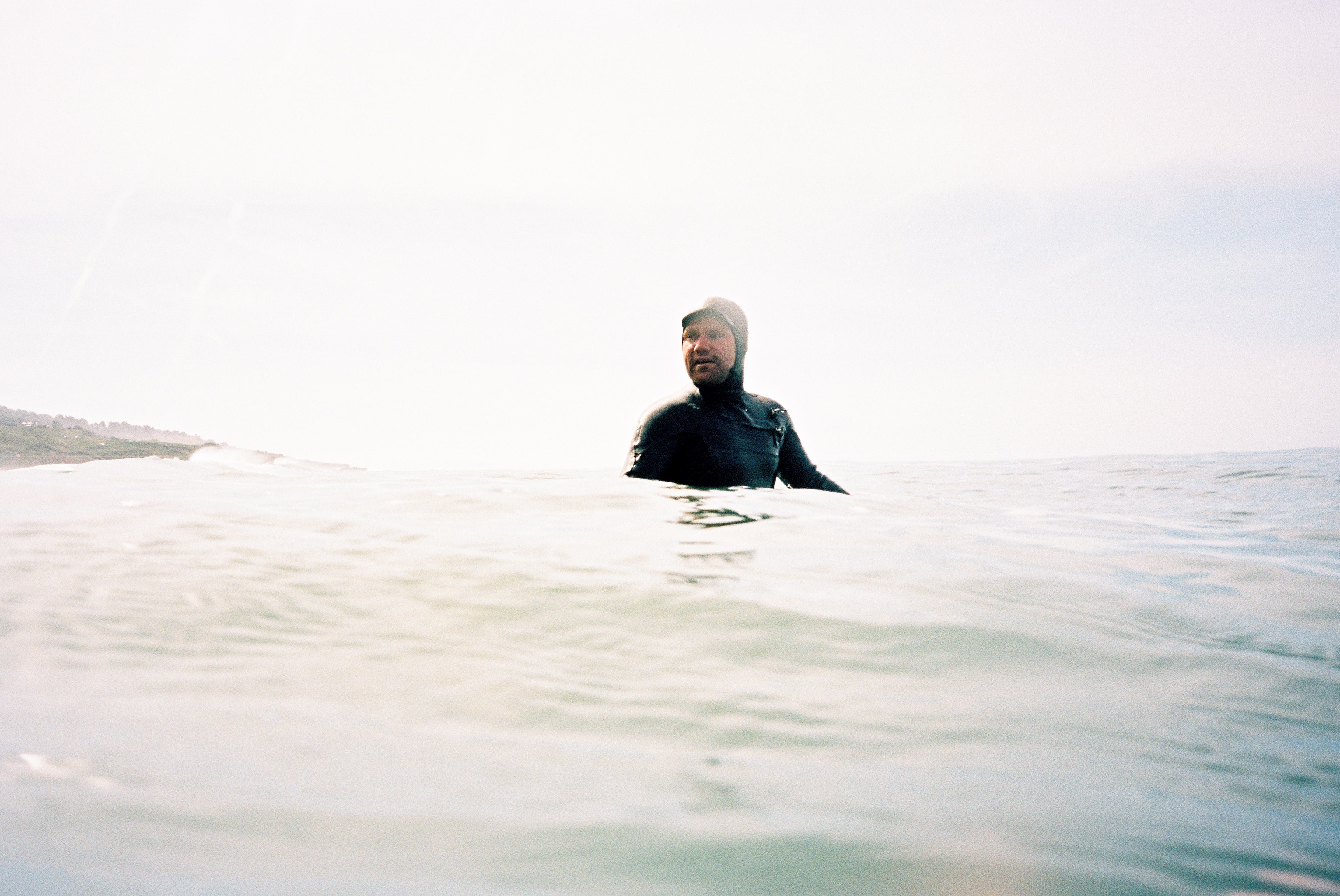 a surfer wearing a wetsuit which comes over his head popping up amidst the waves at santa cruz, glassy mornings 4k, HD Wallpaper