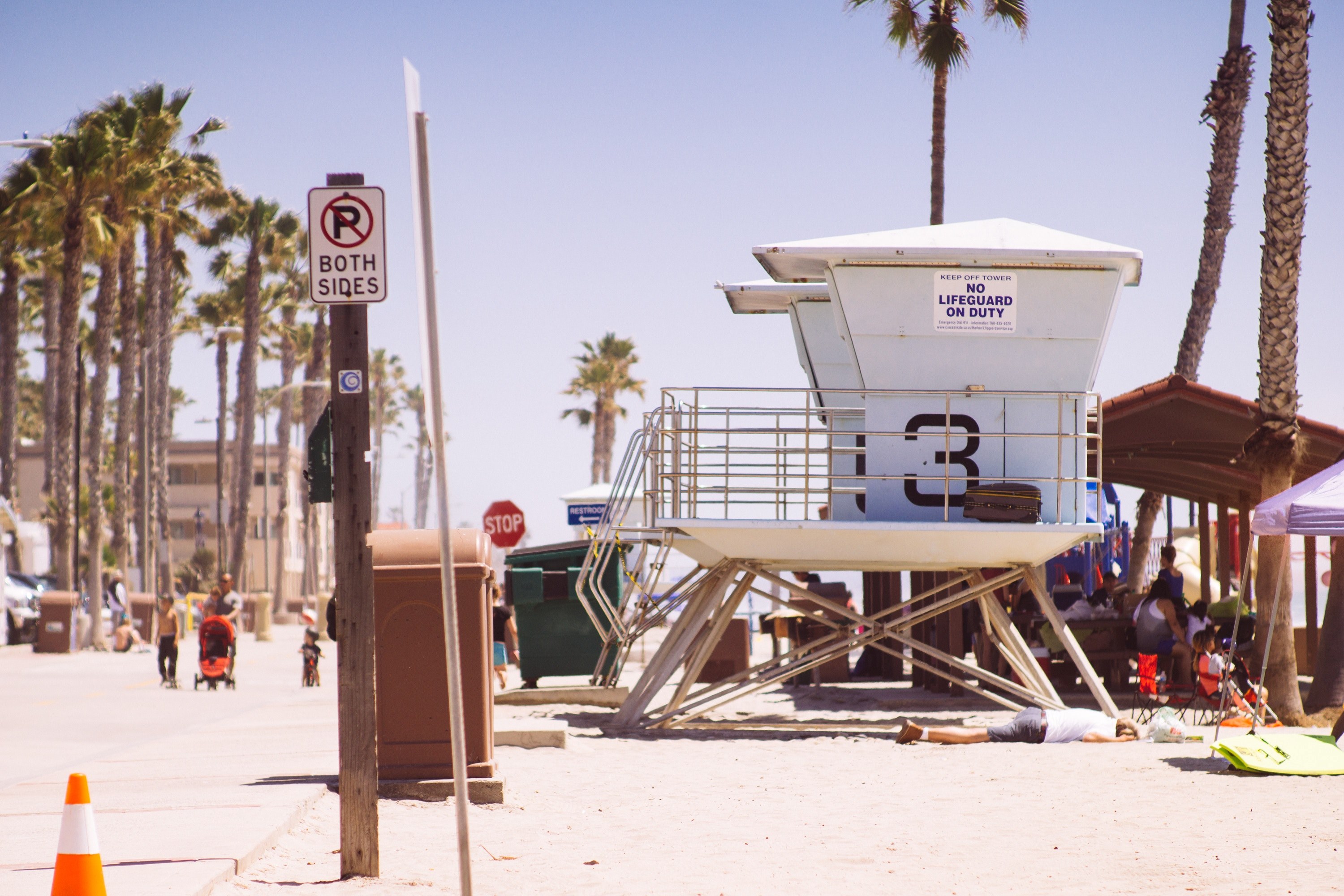 beach premises featuring lifeguard hut palm trees a resting man and pedestrians at oceanside, resting at oceanside beach 4k, HD Wallpaper