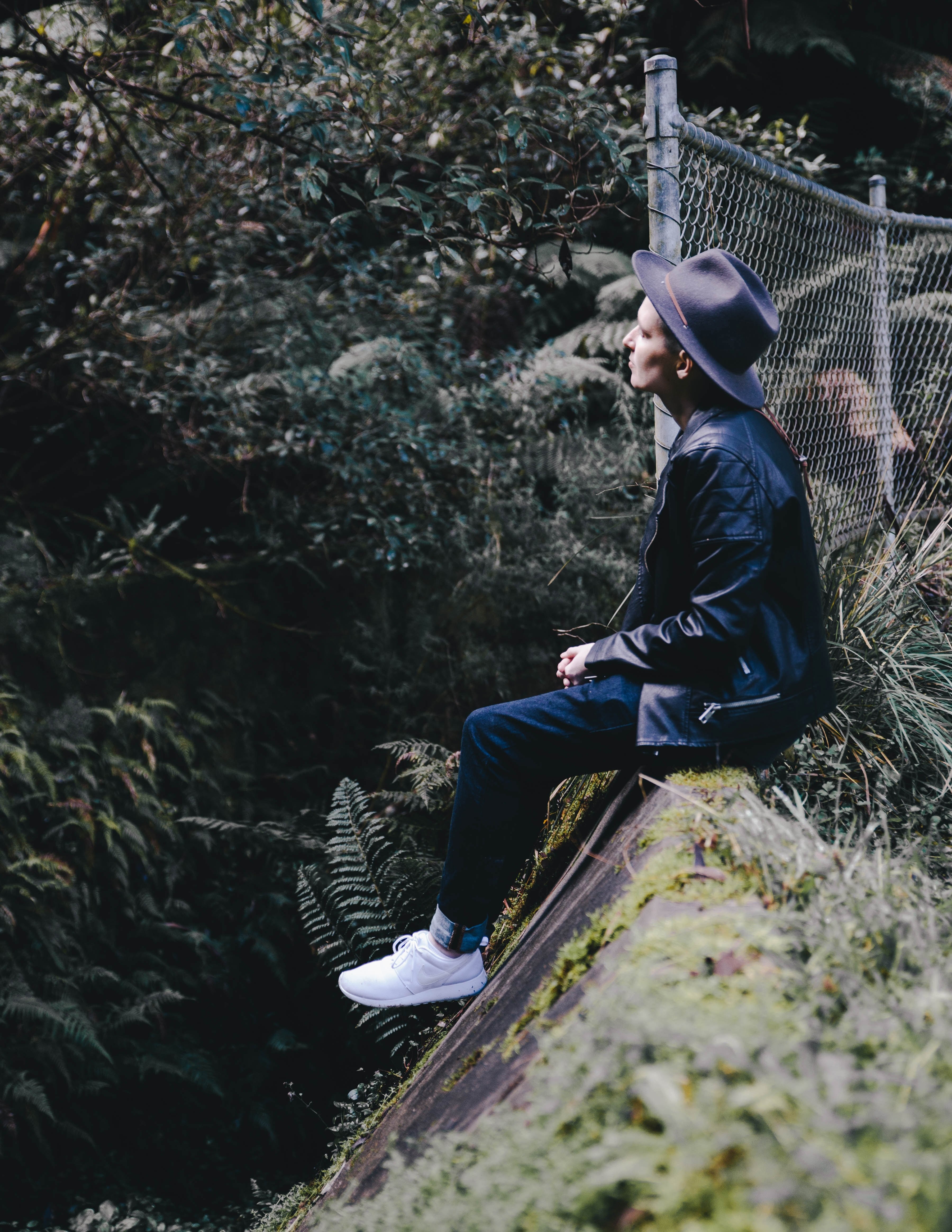 a person in a hat and white sneakers sits by a fence on a steep ledge, person on steep ledge 4k, Phone HD Wallpaper