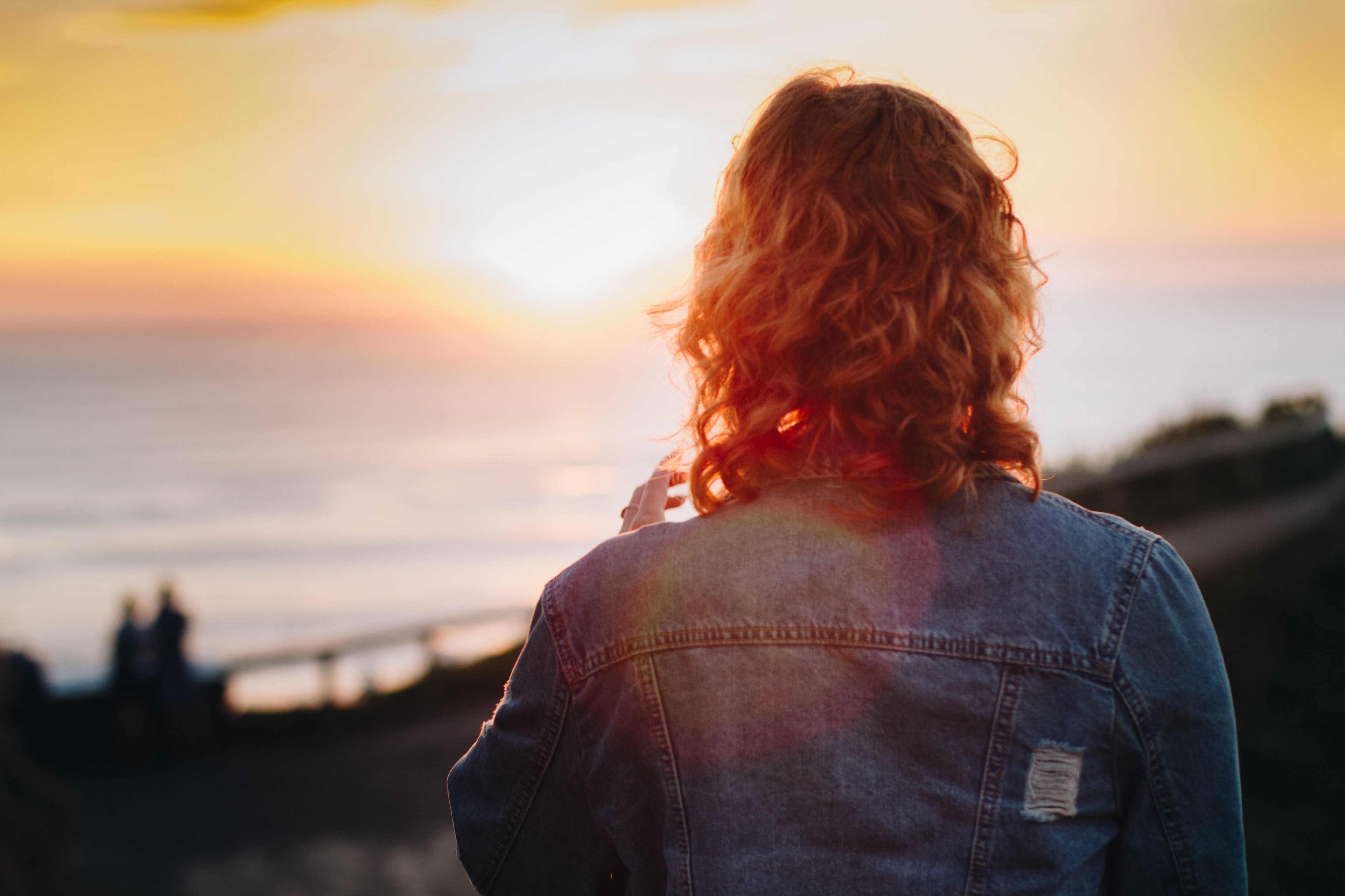 a person with long curly hair and a denim jacket faces the obscure coastal view and sunrise or sunset horizon, fire 4k, HD Wallpaper