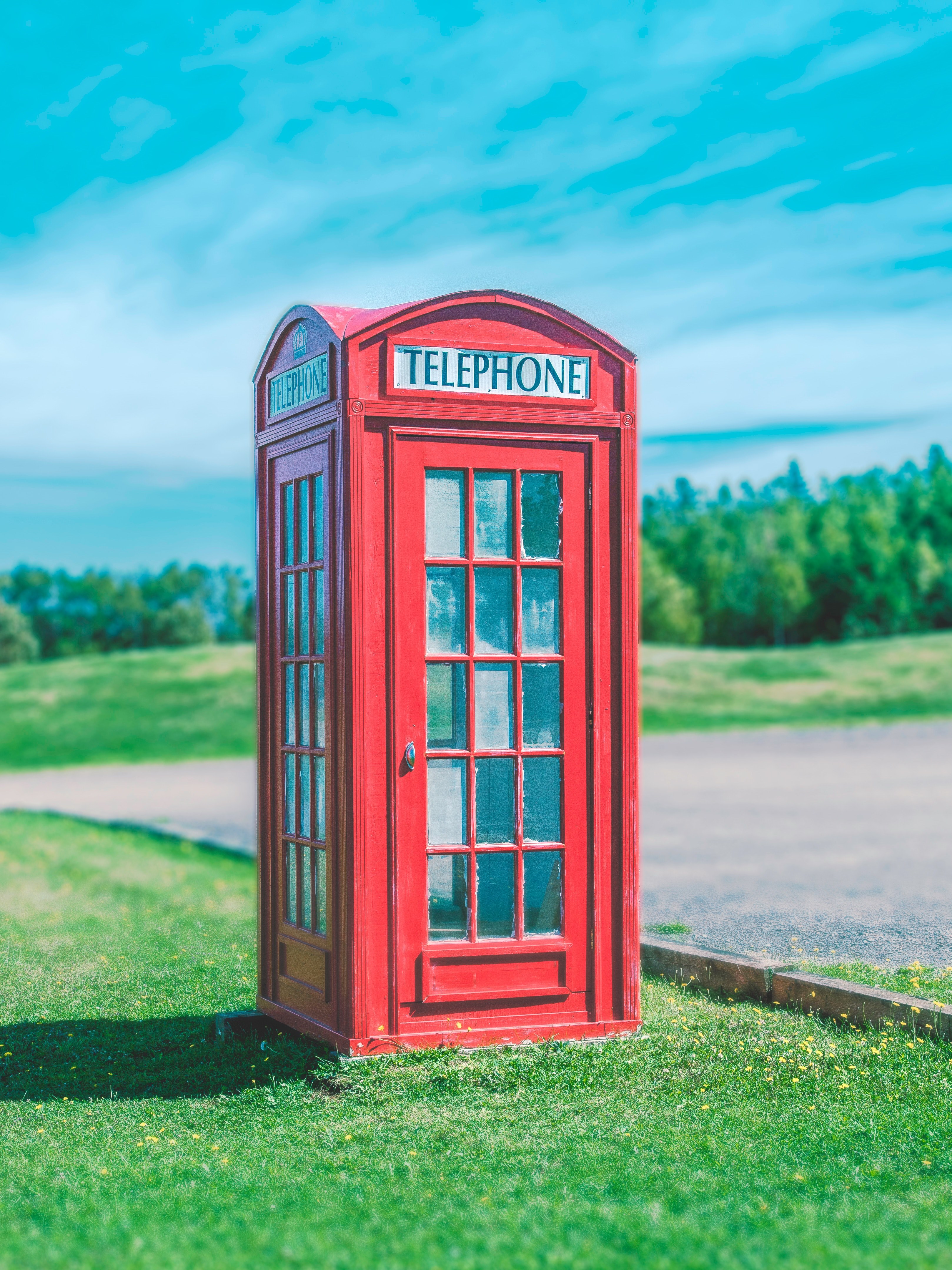a red telephone booth sits on green grass against a blue sky, telephone booth in grass 4k, Phone HD Wallpaper