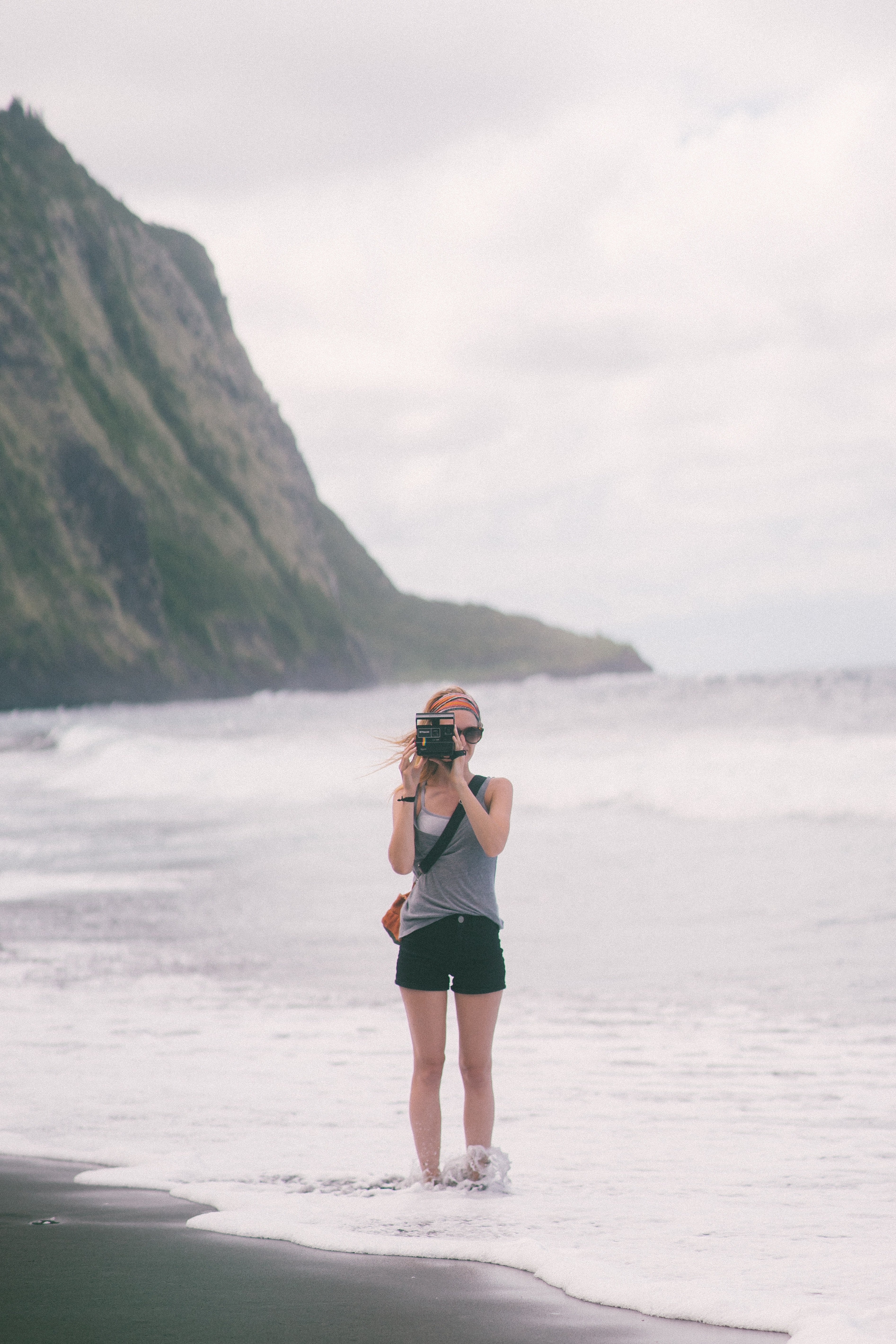 young woman standing on the beach and taking a photo with a polaroid camera, black sands 6 4k, Phone HD Wallpaper