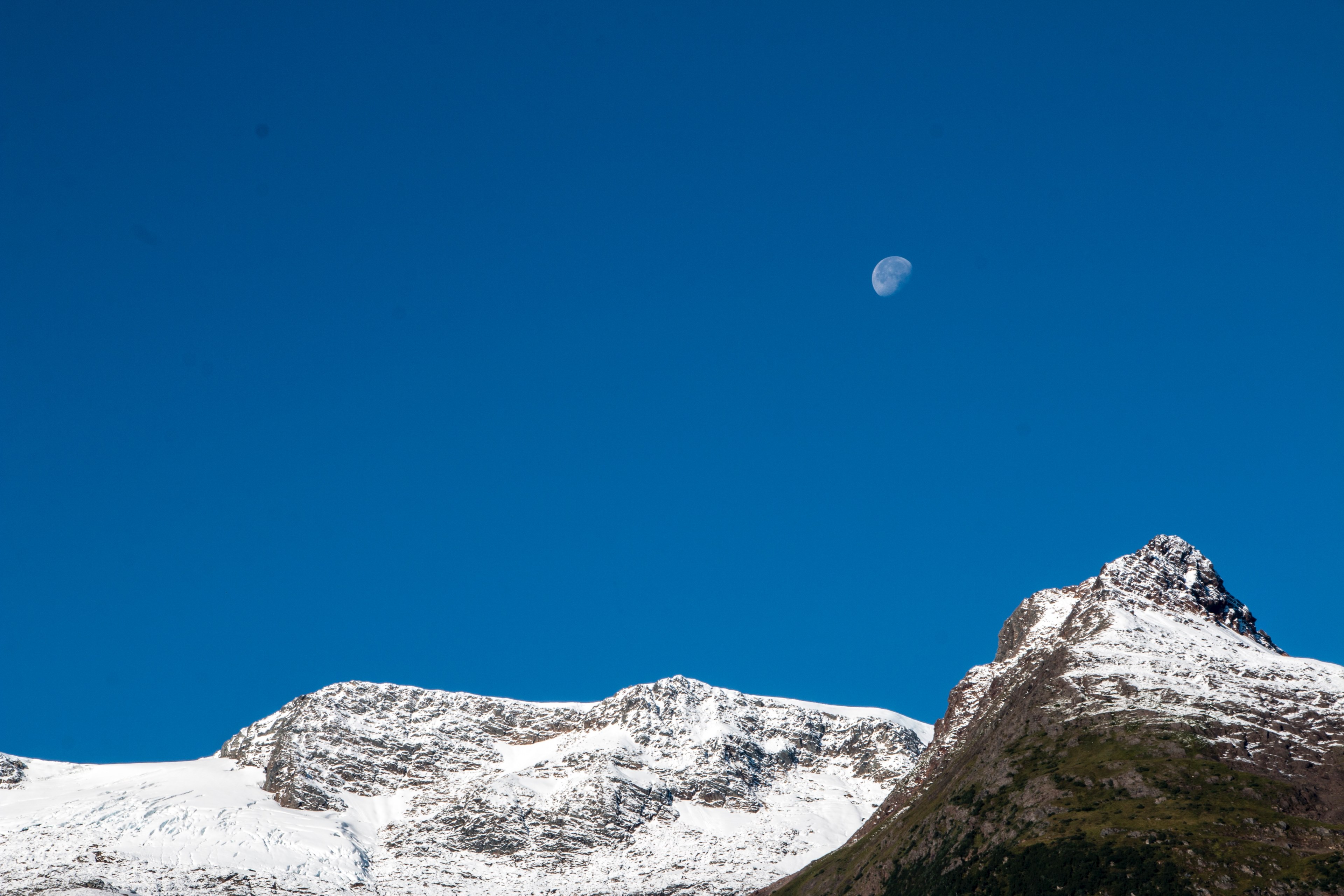 a waning moon in the blue sky above a snow capped mountain ridge, moon above snowy peaks 4k, HD Wallpaper