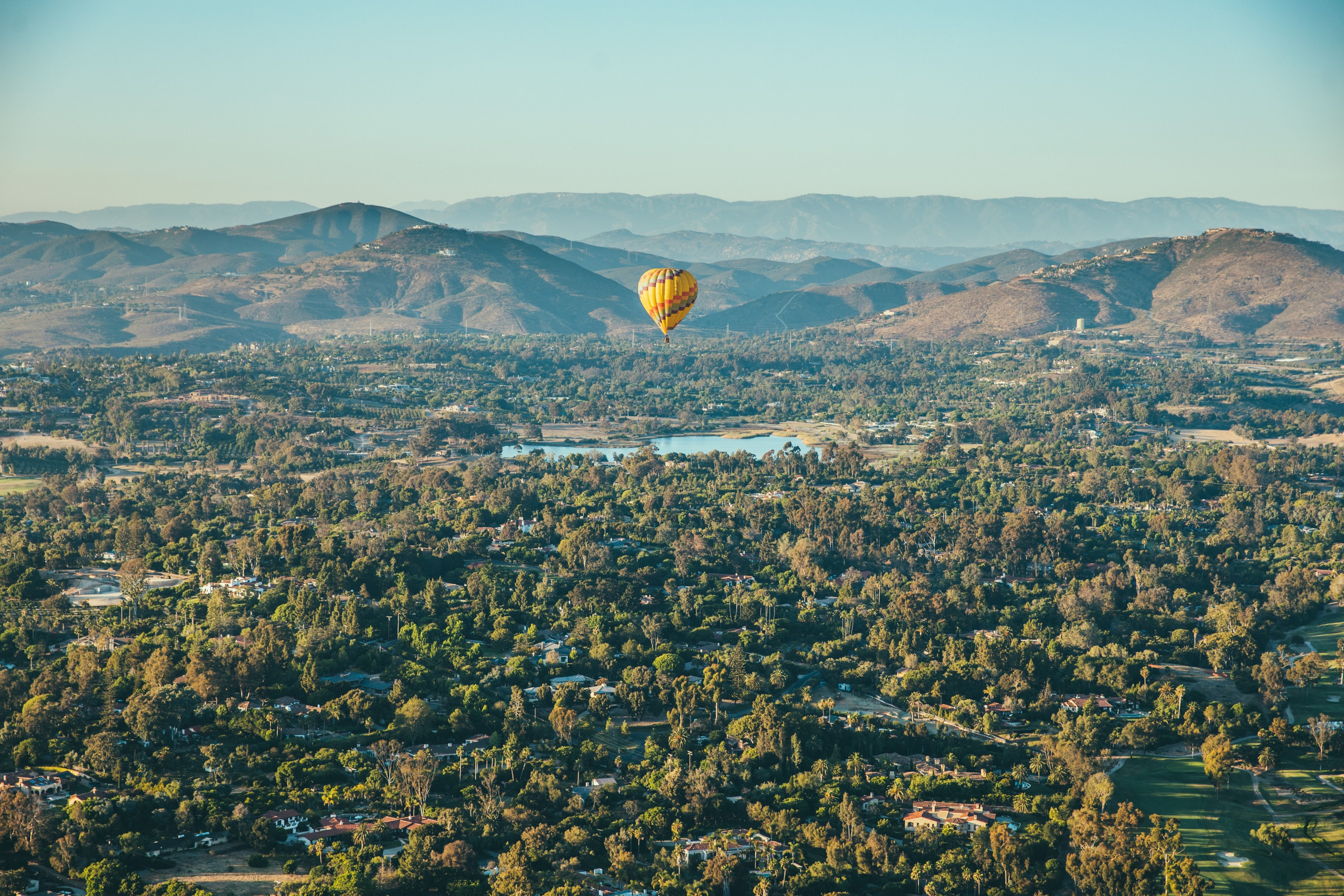 a yellow hot air balloon in the air above a small village among hills, hot air balloon over a village 4k, HD Wallpaper