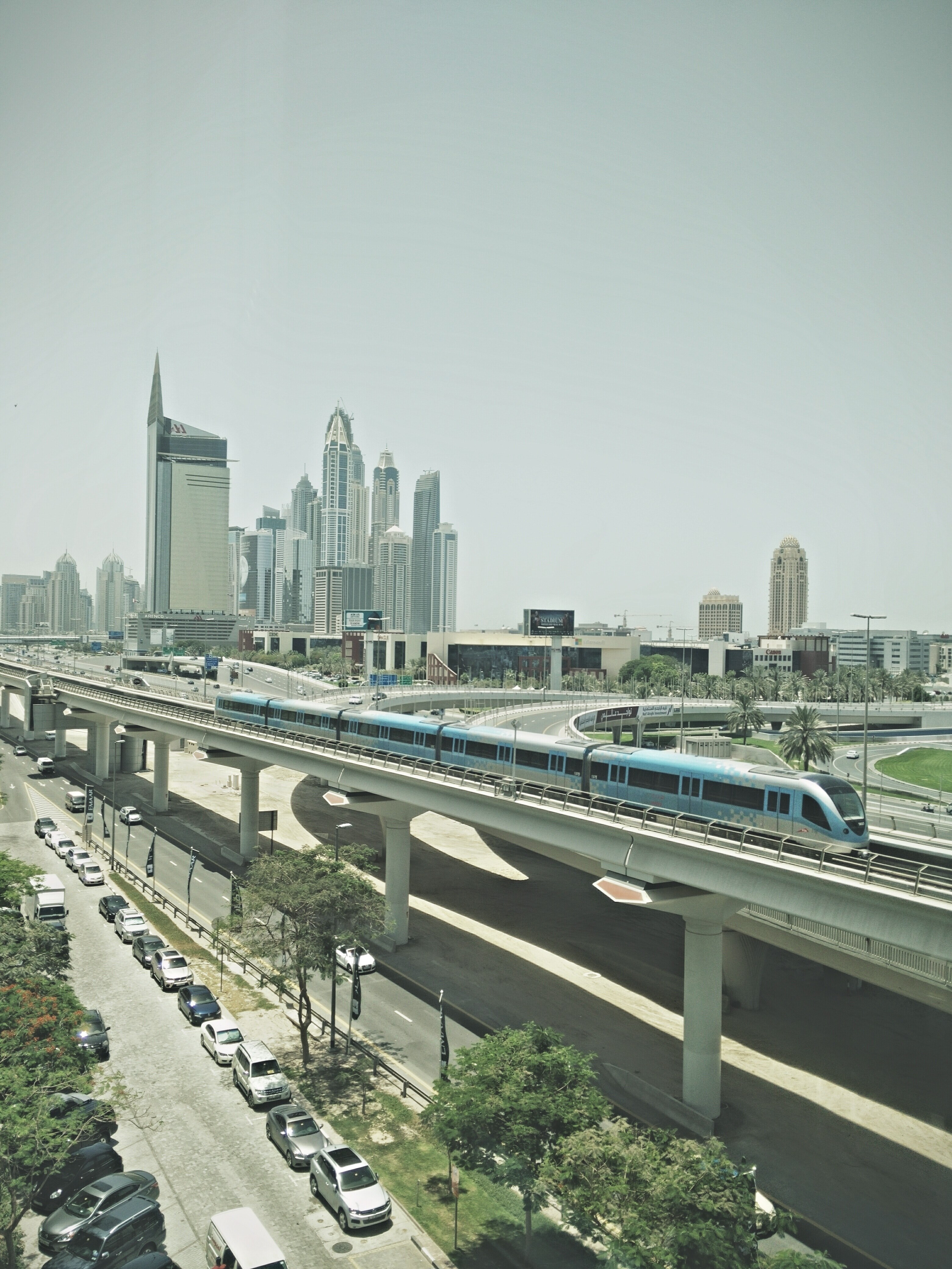 train on bridge in dubai with city skyscrapers in background and cars parked on pavement below, a day in the city in dubai 4k, Phone HD Wallpaper