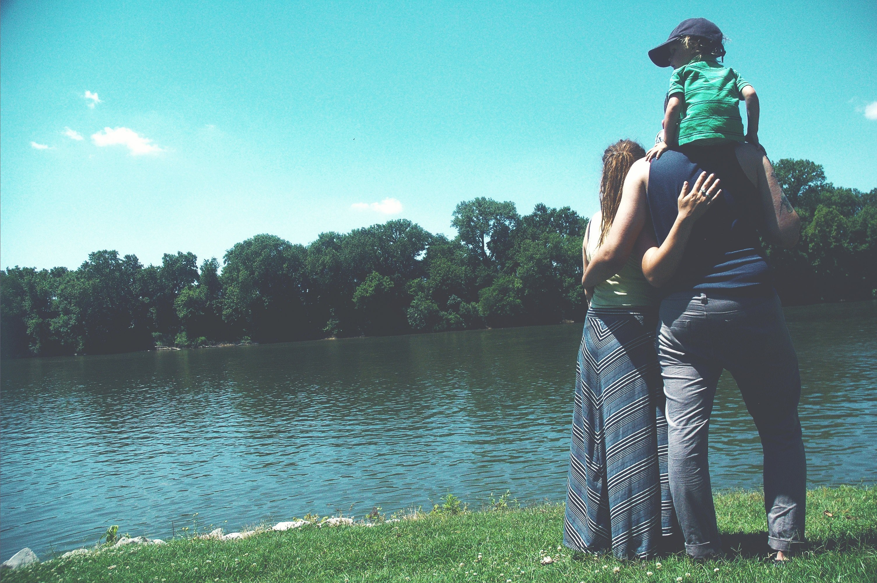 child sitting on the shoulders of father and his parents looking towards a clarksville lake, family standing by lake 4k, HD Wallpaper