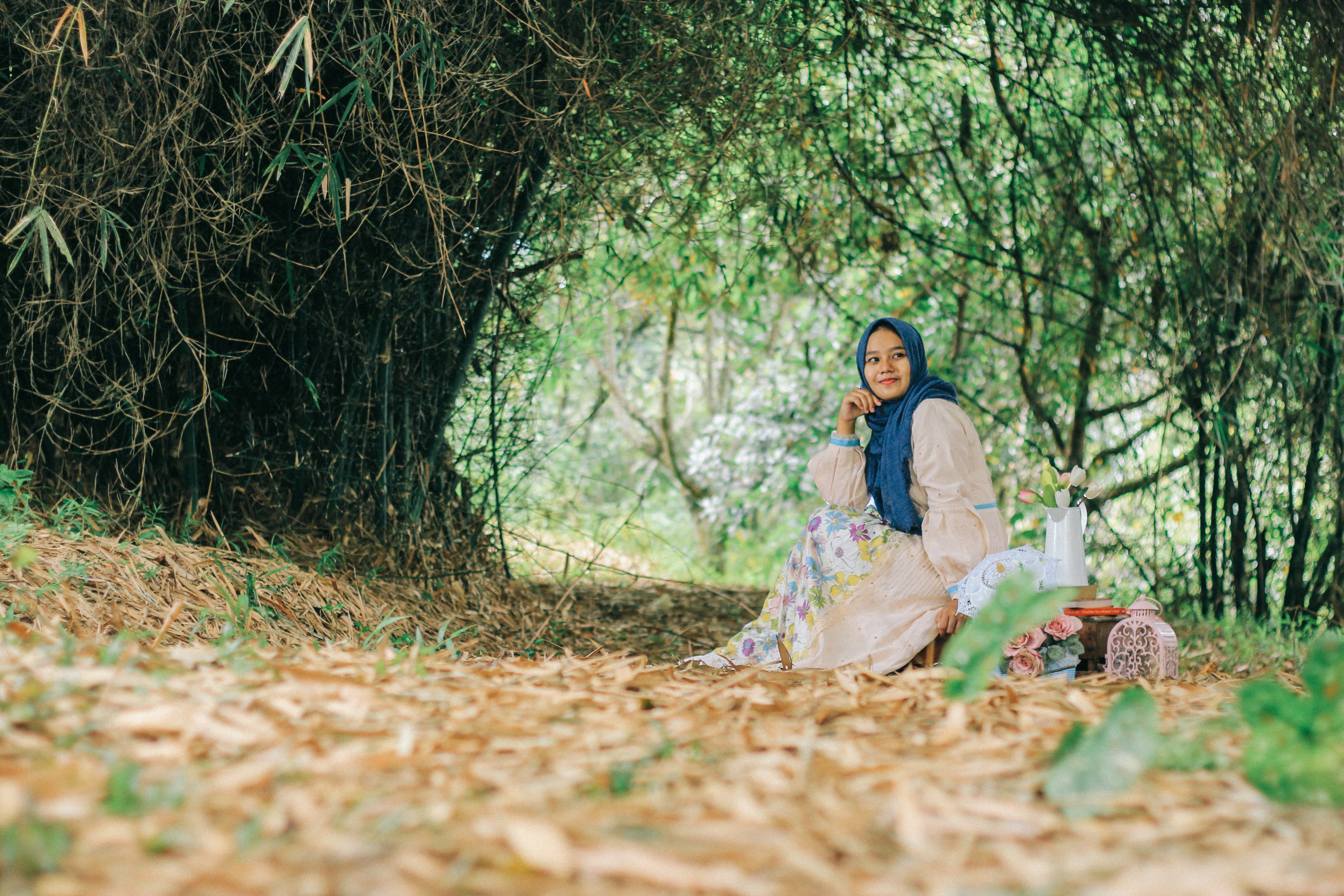 a woman in a blue headscarf and a floral dress smiles while sitting under a green arch, woman in a headscarf resting outdoors 4k, HD Wallpaper