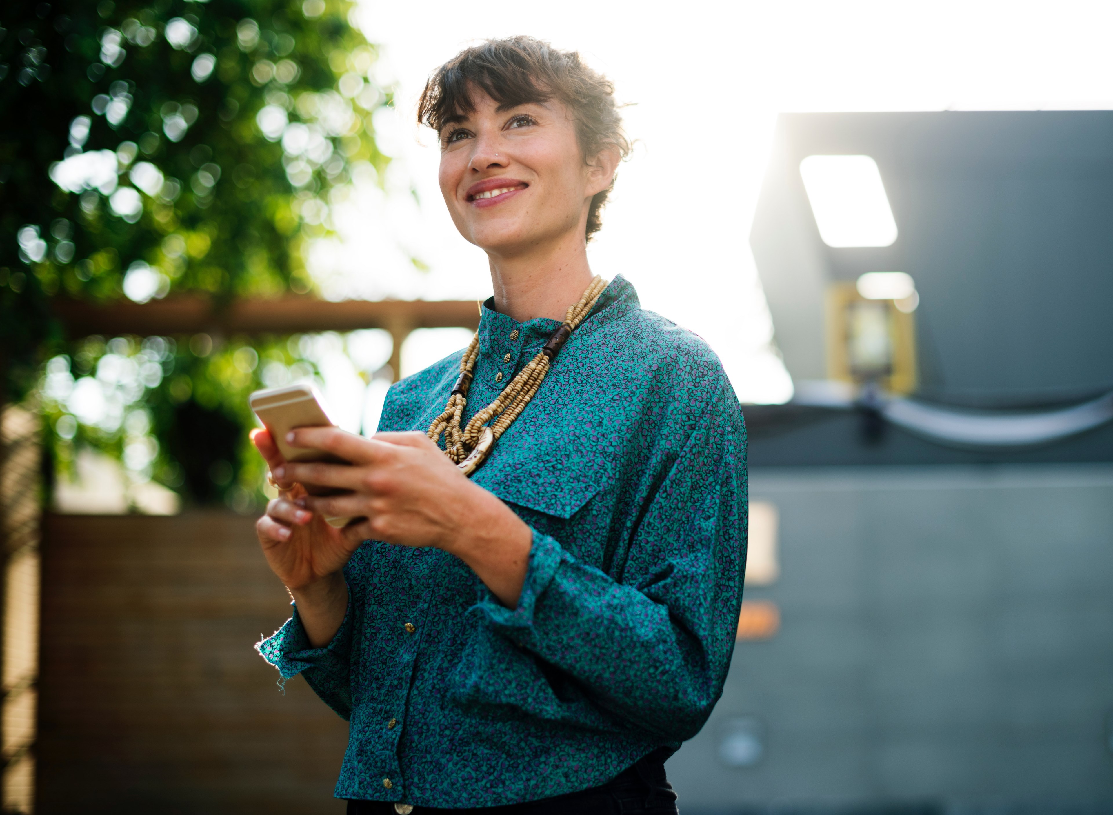 a smiling woman in an azure blouse holding a smartphone while standing outdoors, smiling woman with a phone 4k, HD Wallpaper