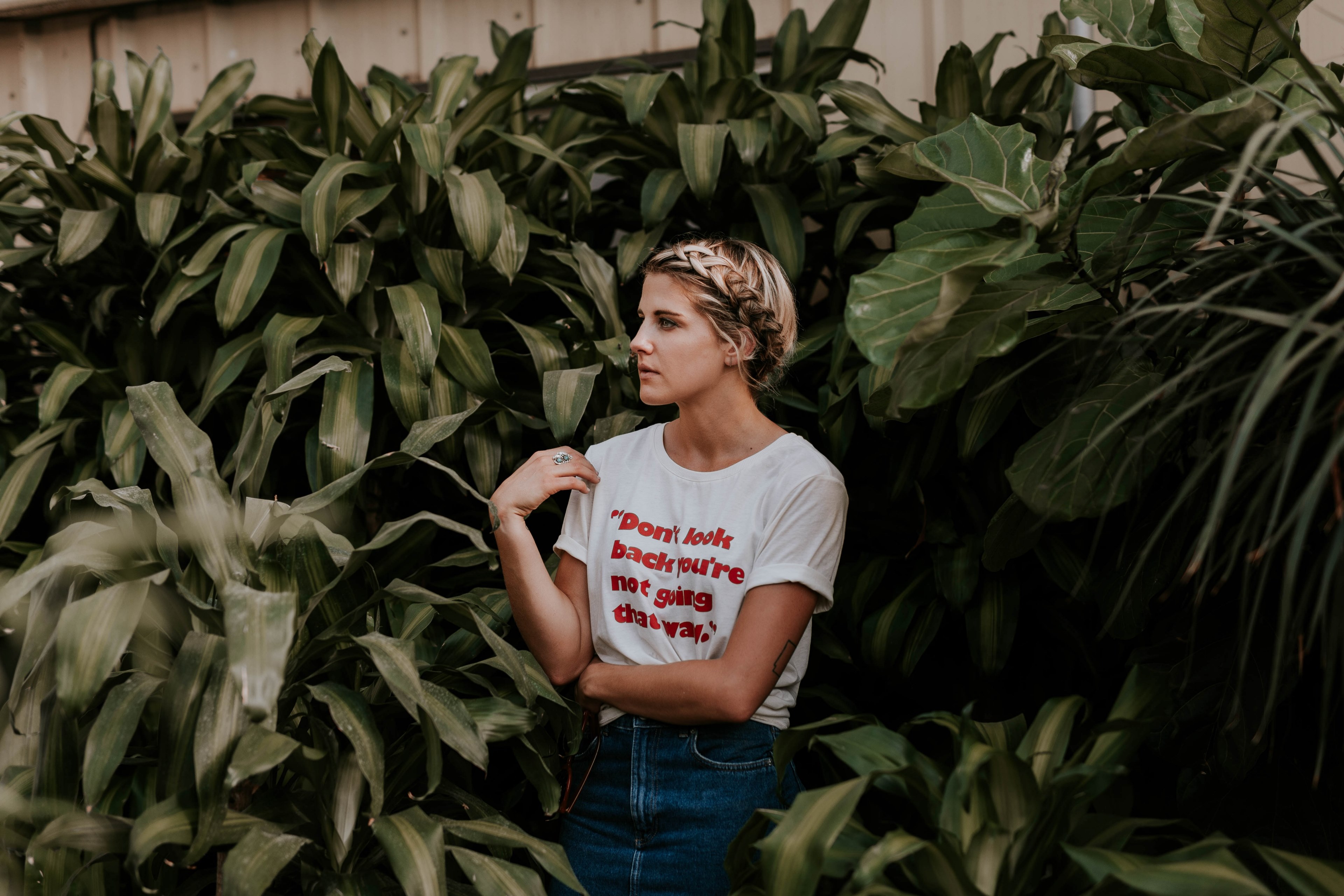 a woman with a braid places her hand on her shoulder looking away among green plants, woman with hand on shoulder 4k, HD Wallpaper