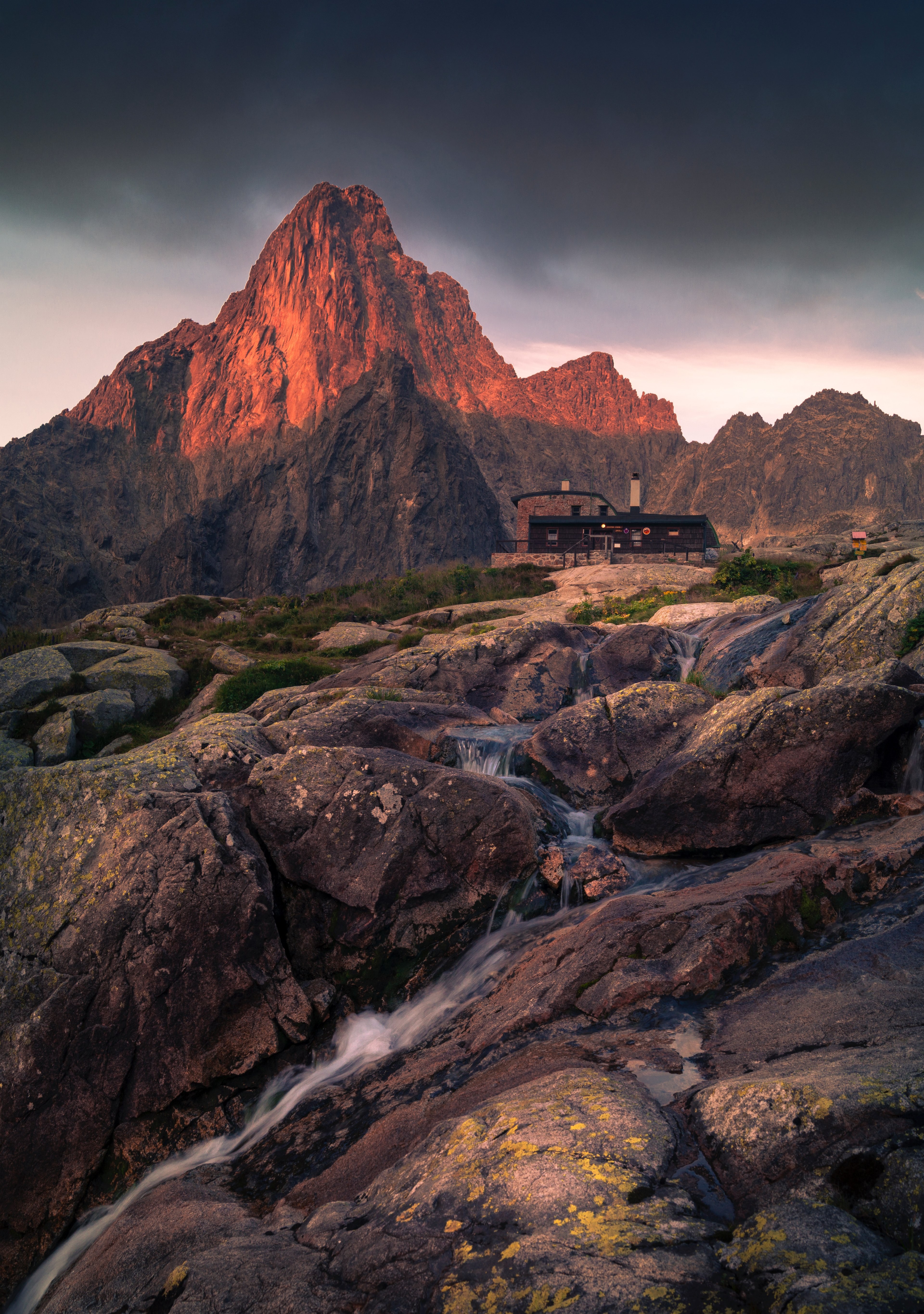 modern house at the top of a rocky hill with mountains and a creek in the background and foreground during sunset, house in the mountain 4k, Phone HD Wallpaper