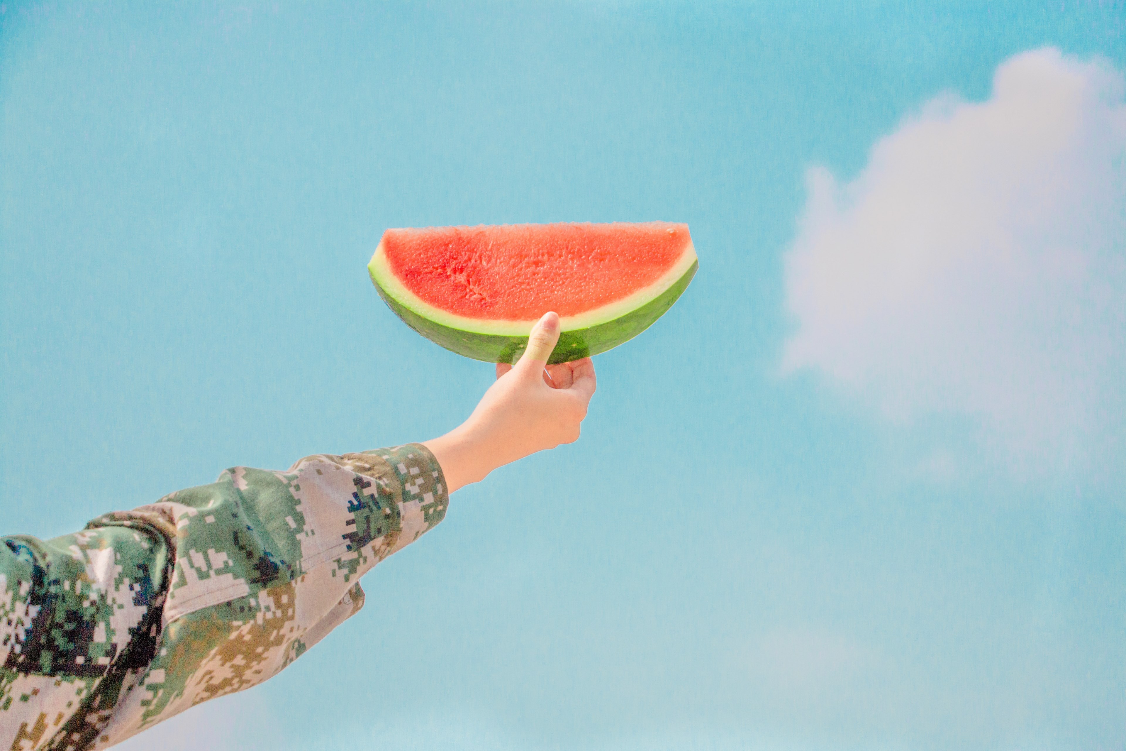 person wearing a camo holds a piece of watermelon to the blue sky, watermelon sky arm and camo 4k, HD Wallpaper