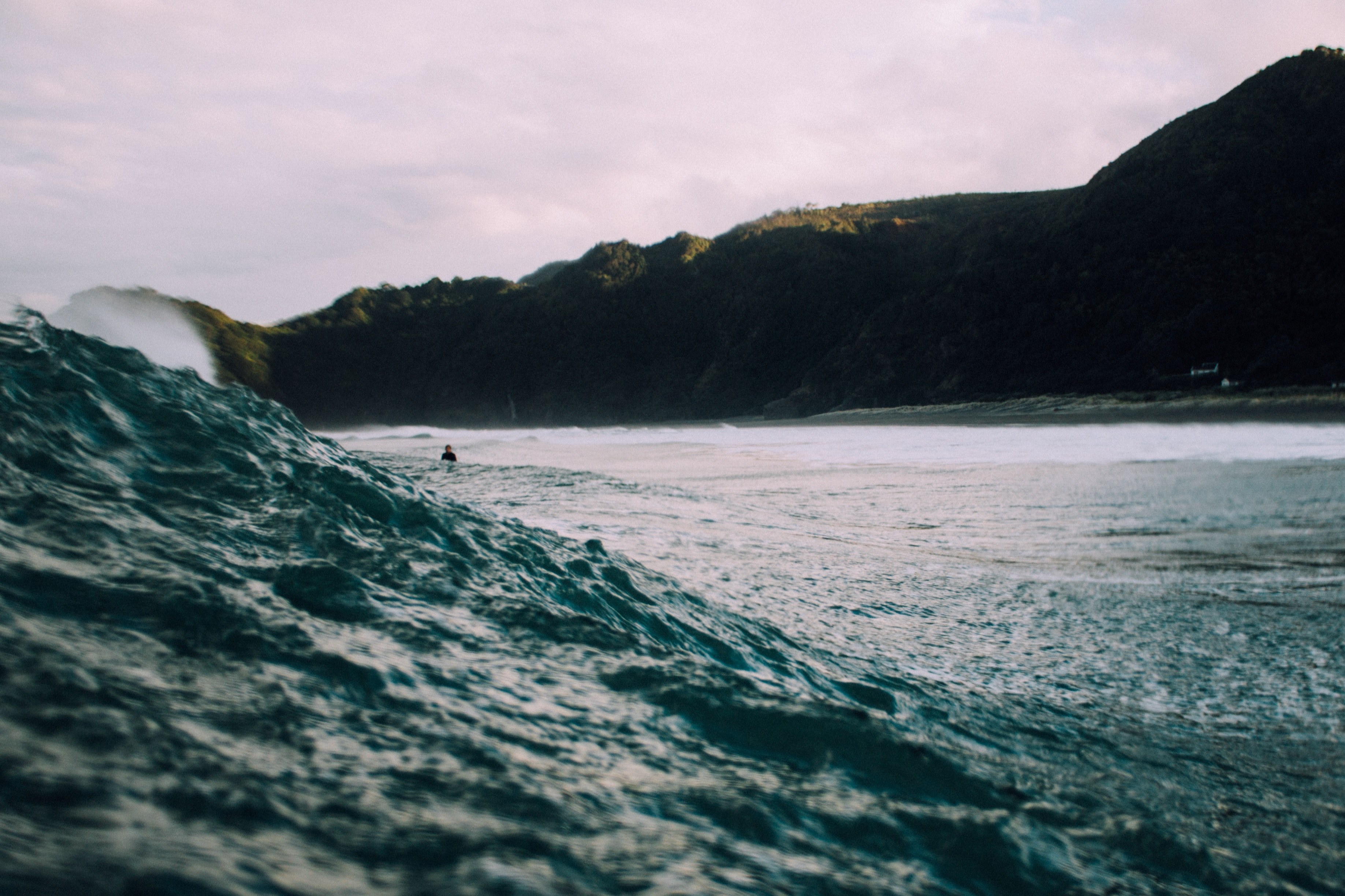 a shot of a rolling wave with a surfer in the distance and the mountains in the background at piha, surfing in the shadow of the mountains 4k, HD Wallpaper