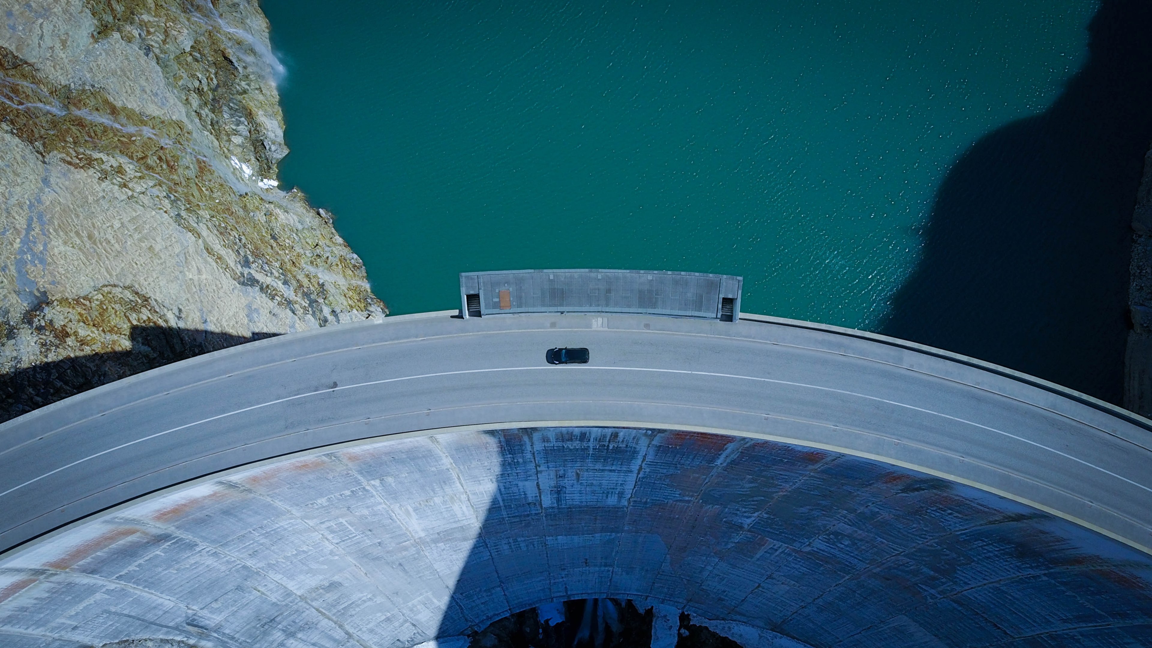 a drone shot of a car driving along a curve in a road on a tall dam in tignes, on the road again 4k, HD Wallpaper