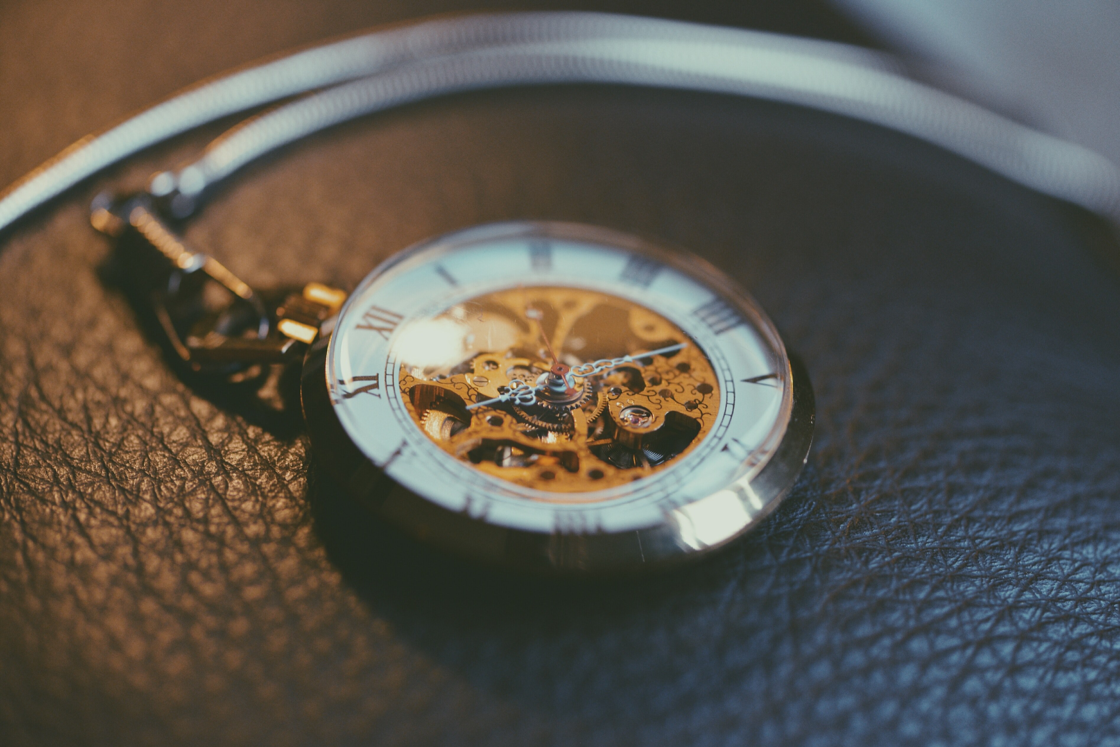 an intricate pocket watch showing roman numerals and a complex gear system behind the hands resting on a leather piece of furniture, timepiece on leather 4k, HD Wallpaper