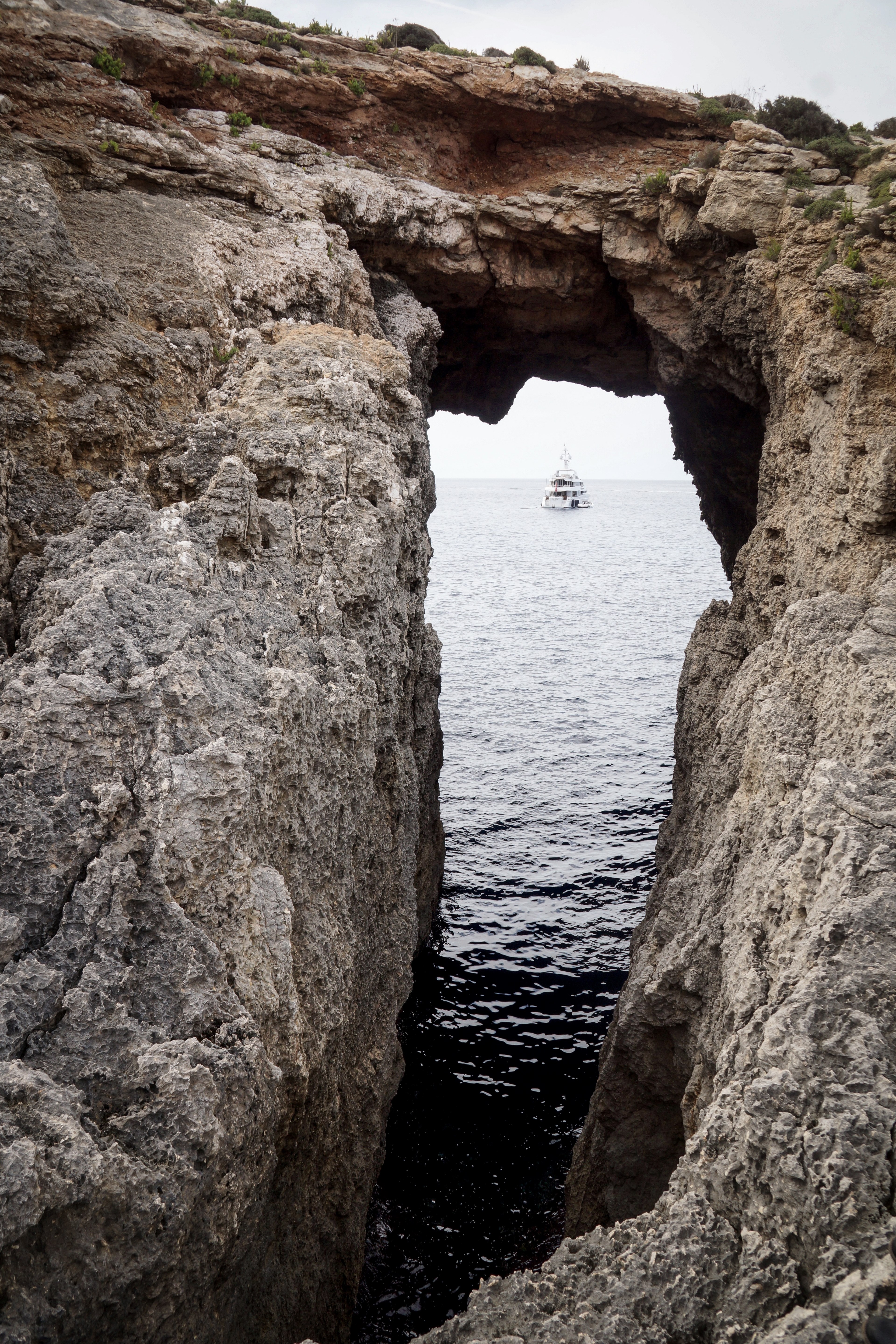 a view of a boat on sea through an opening in an arched rock formation, boat under a rocky arch 4k, Phone HD Wallpaper