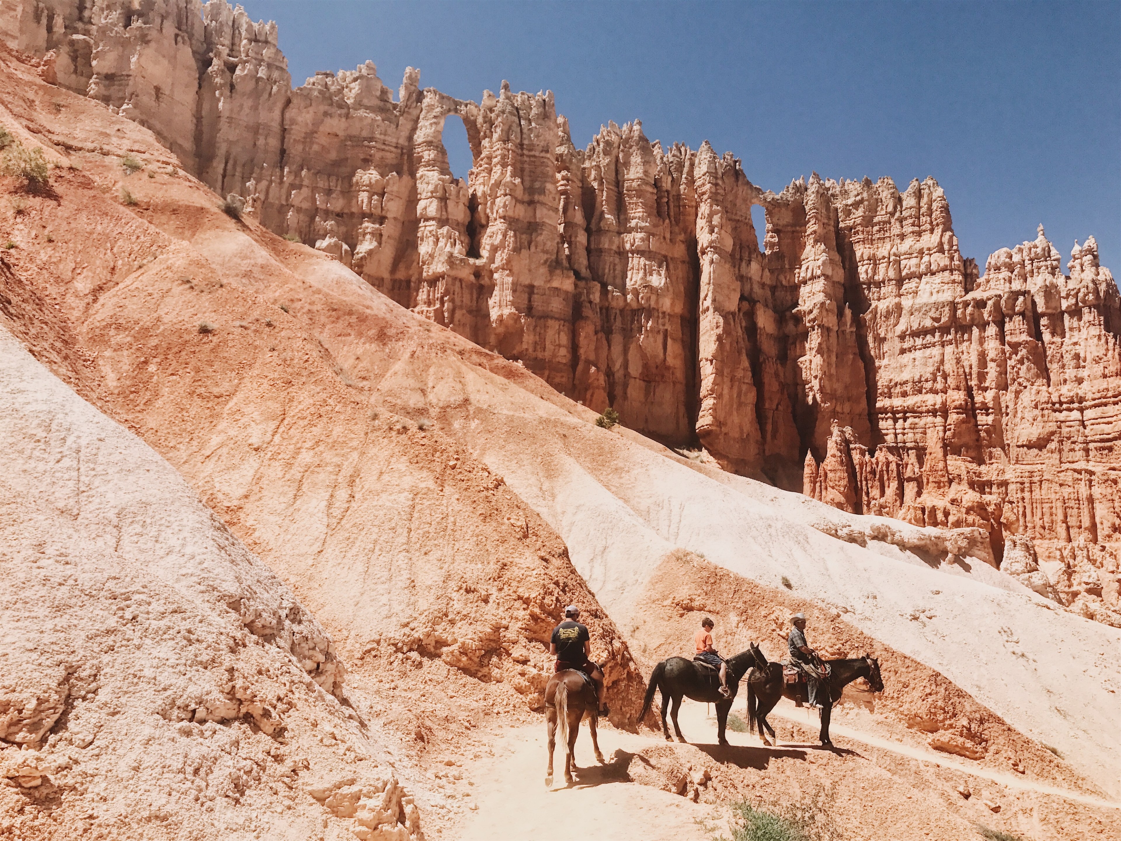 three horse riders going down a steep slope under red sandstone outcroppings, down the red slope on horseback 4k, HD Wallpaper