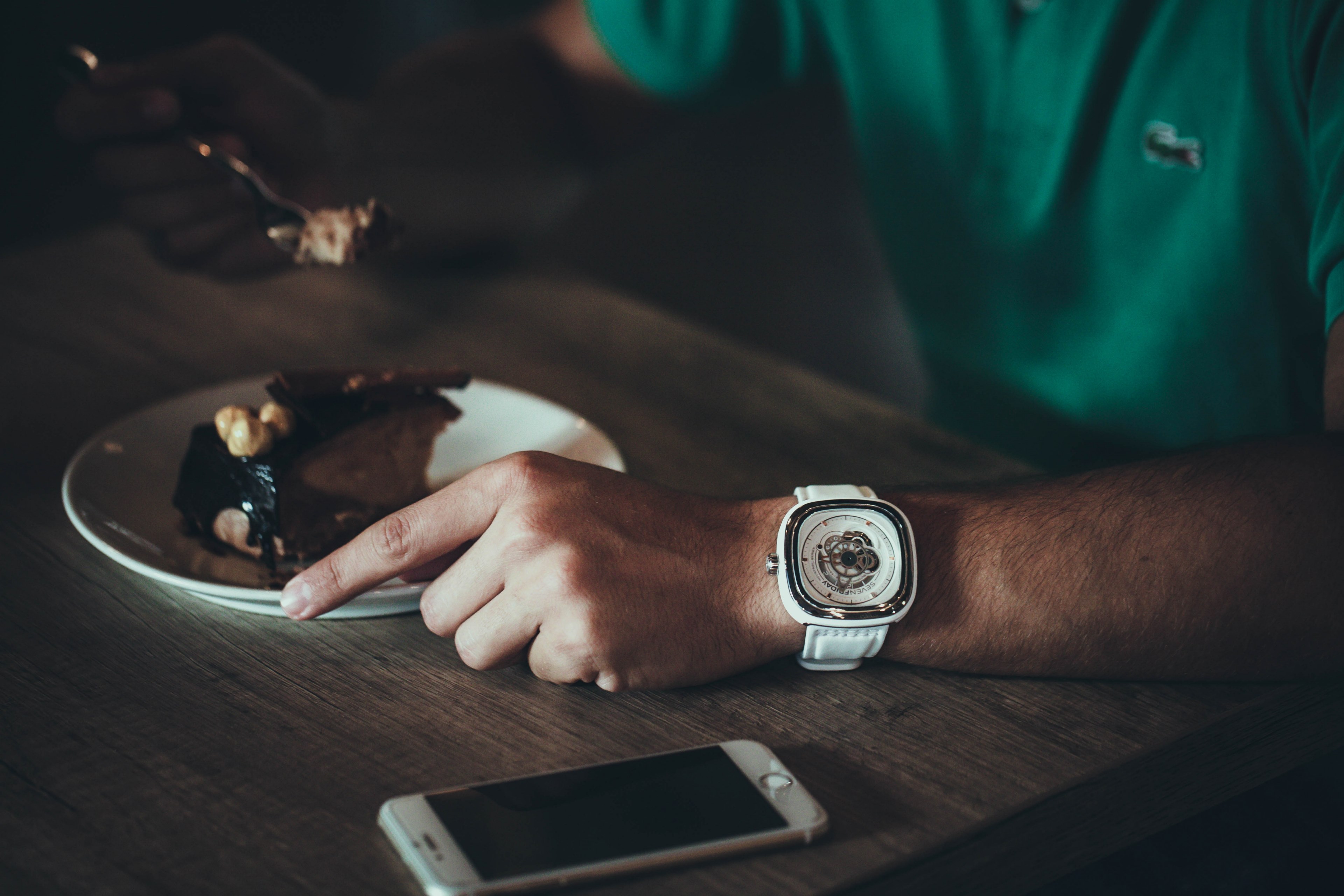 a man wearing a white watch and green shirt eating a slice of cake at a cafe while his iphone cellphone sits nearby on the table in switzerland, eating dessert 4k, HD Wallpaper