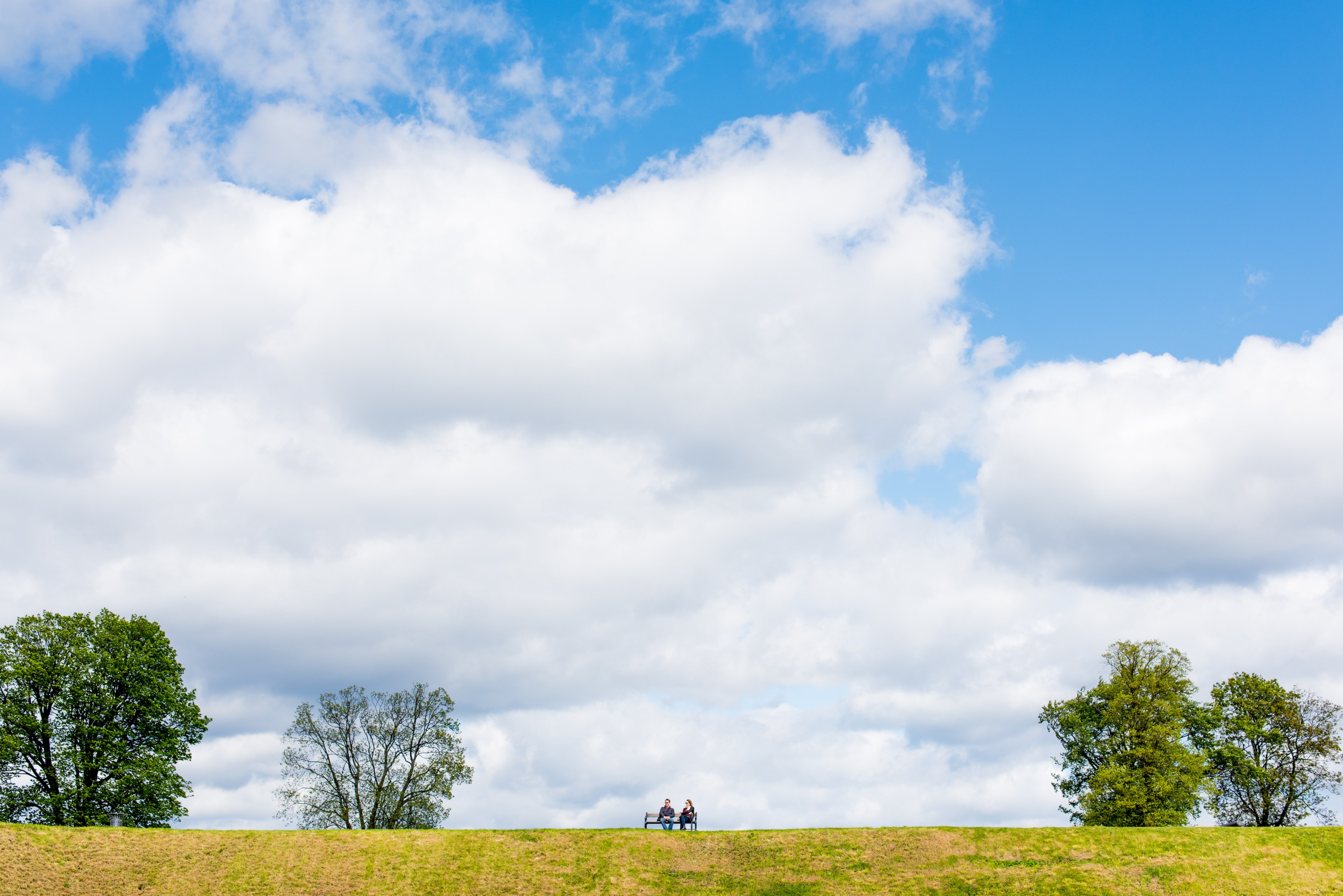 a distant shot of two people sitting on a bench under heavy clouds, a couple on a bench in the distance 4k, HD Wallpaper
