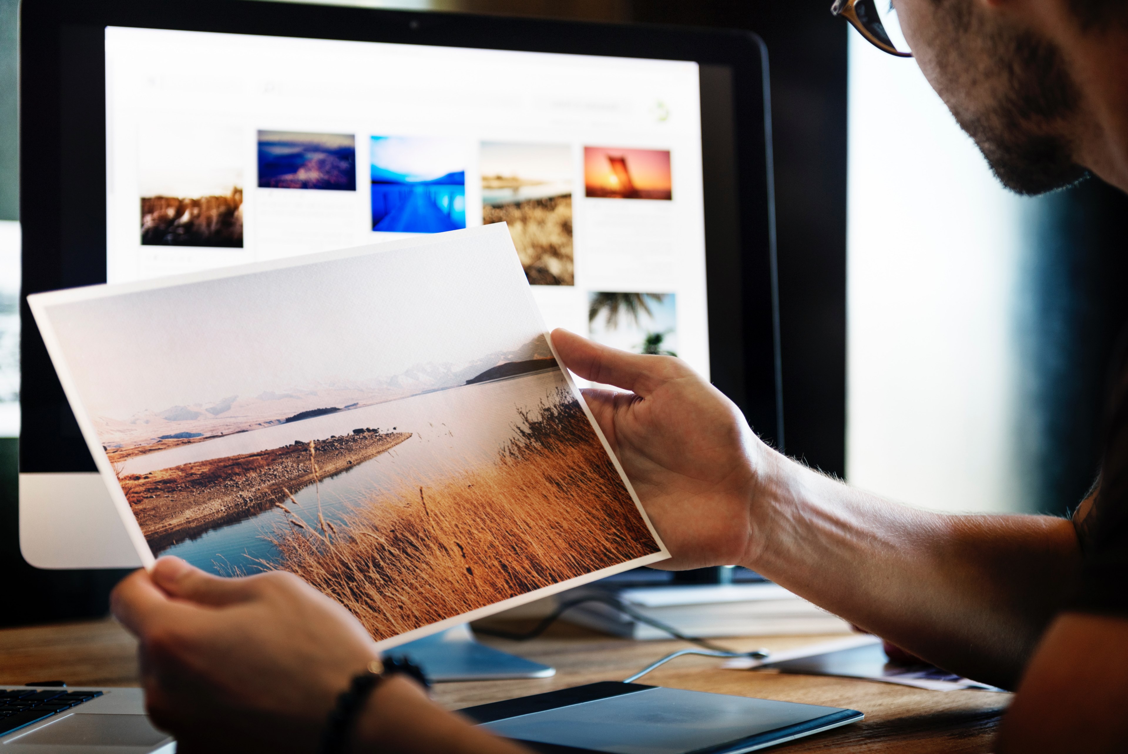 man wearing glasses holding printed photo in front of computer work space, man holding river photo 4k, HD Wallpaper