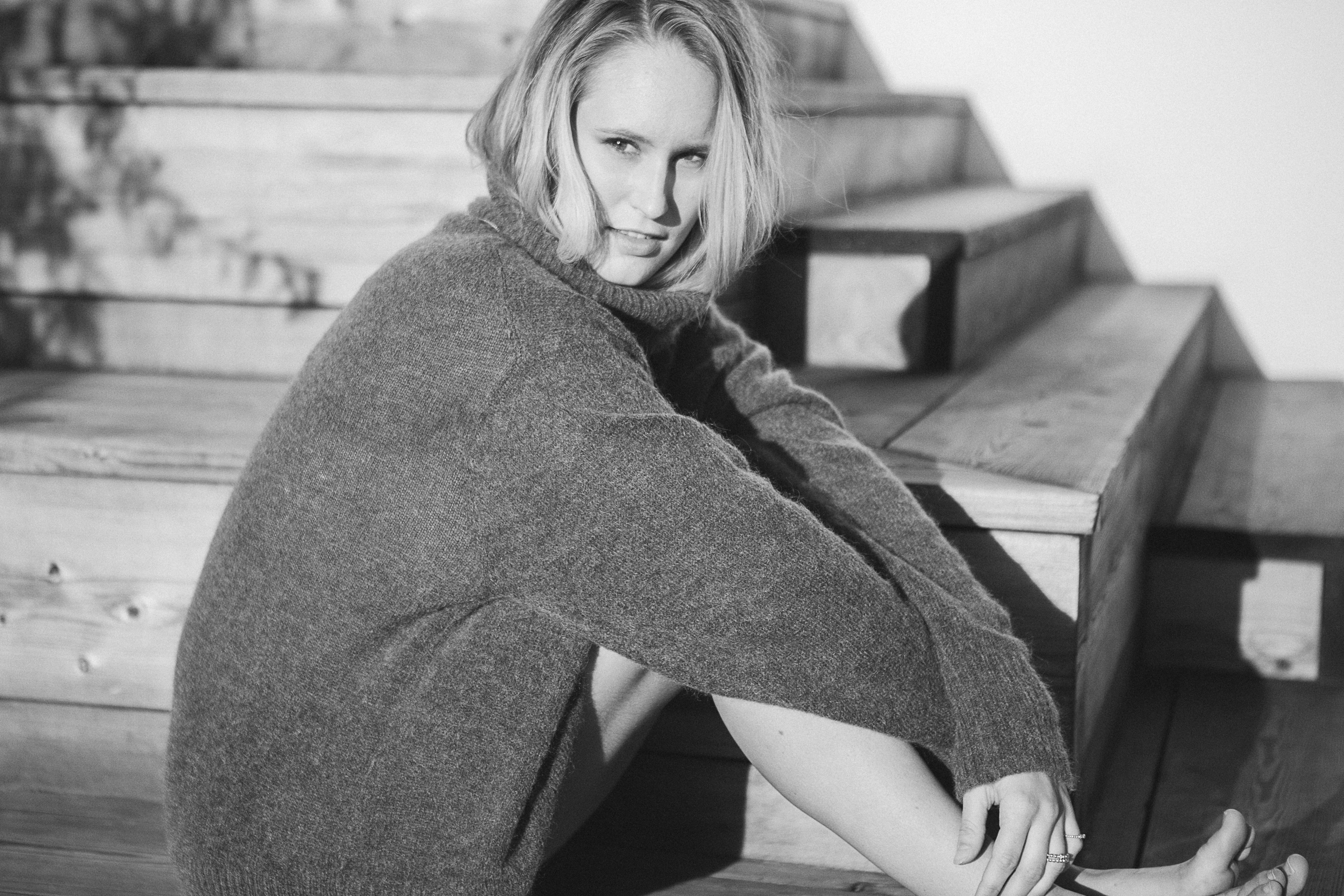 a black and white woman in a large sweater sits aside wooden stairs, woman aside wooden stairs 4k, HD Wallpaper