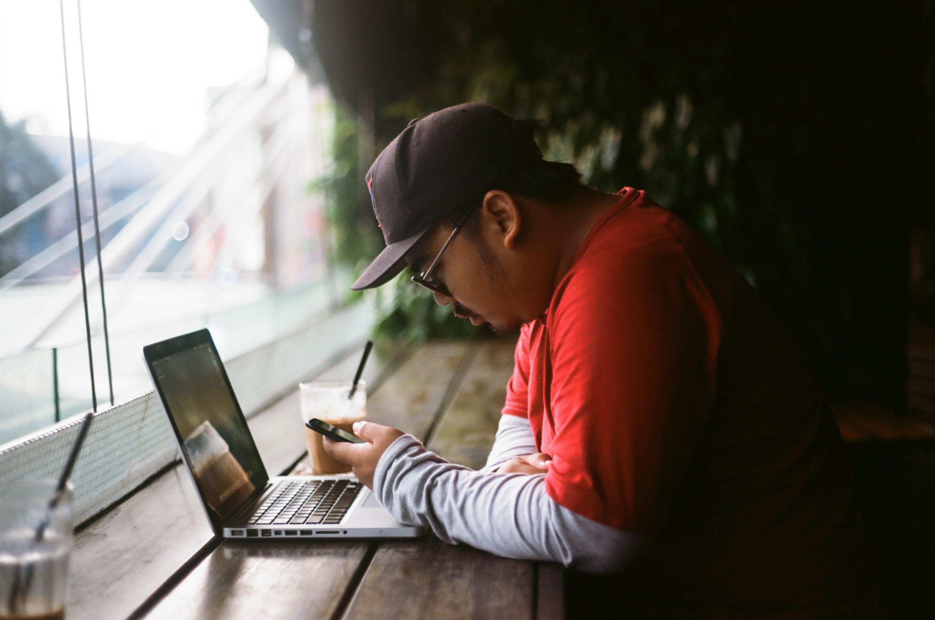 a man sits with a laptop at a cafe table in jakarta using his cell phone, man sitting with laptop 4k, HD Wallpaper